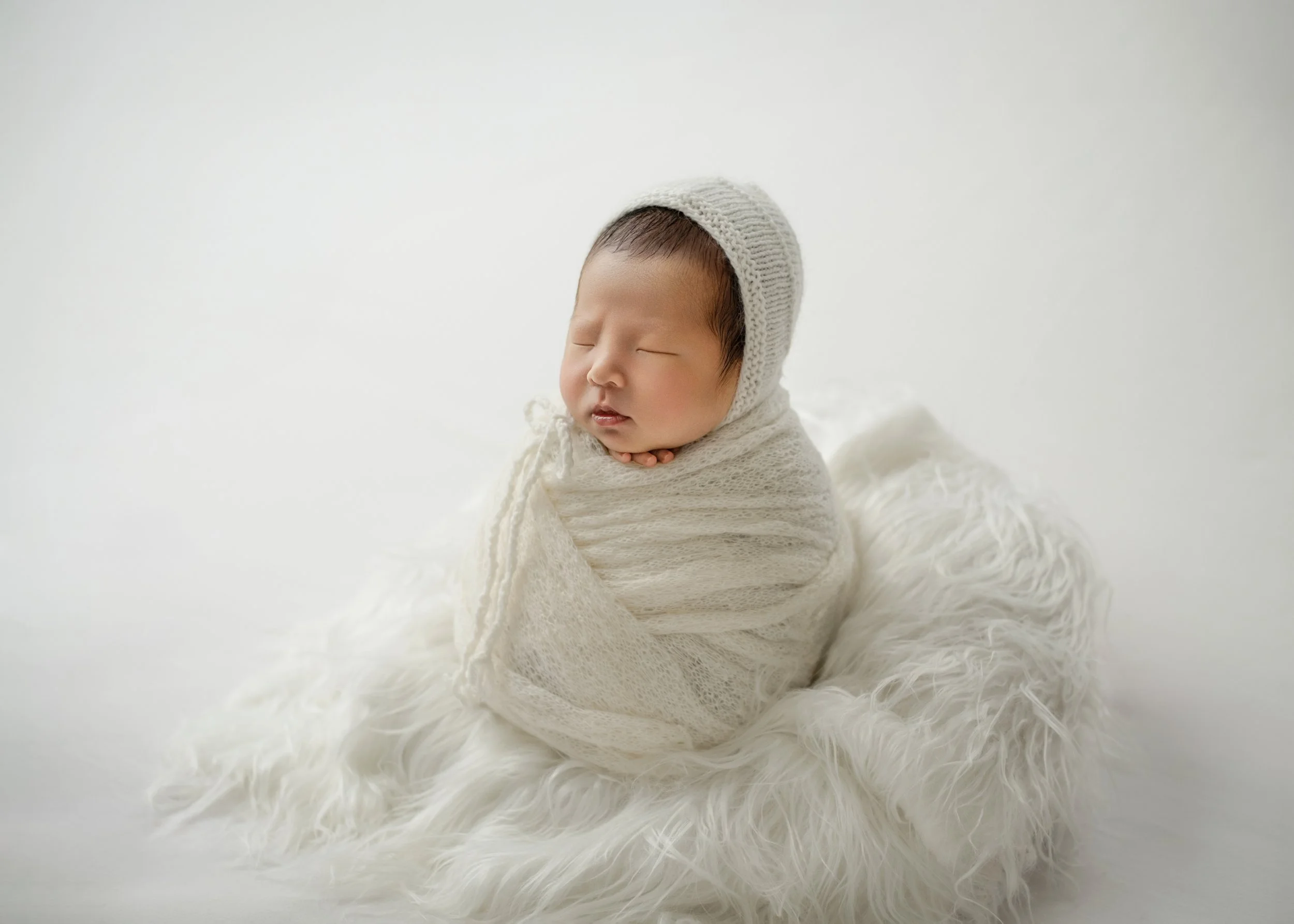 白い毛糸のおくるみに包まれた新生児の赤ちゃんが静かに眠っている。