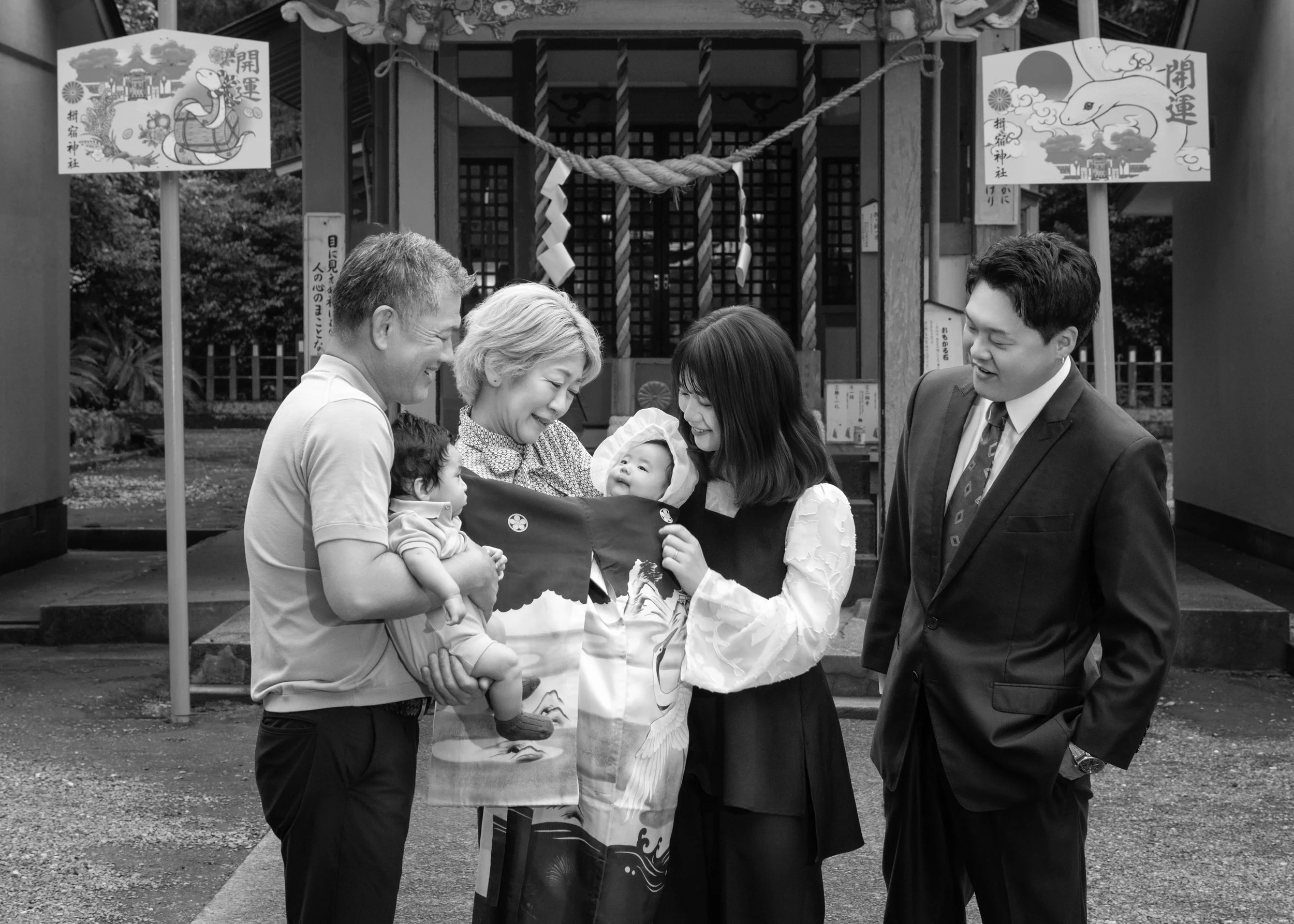 家族が神社の前で赤ちゃんの祝いをしている光景