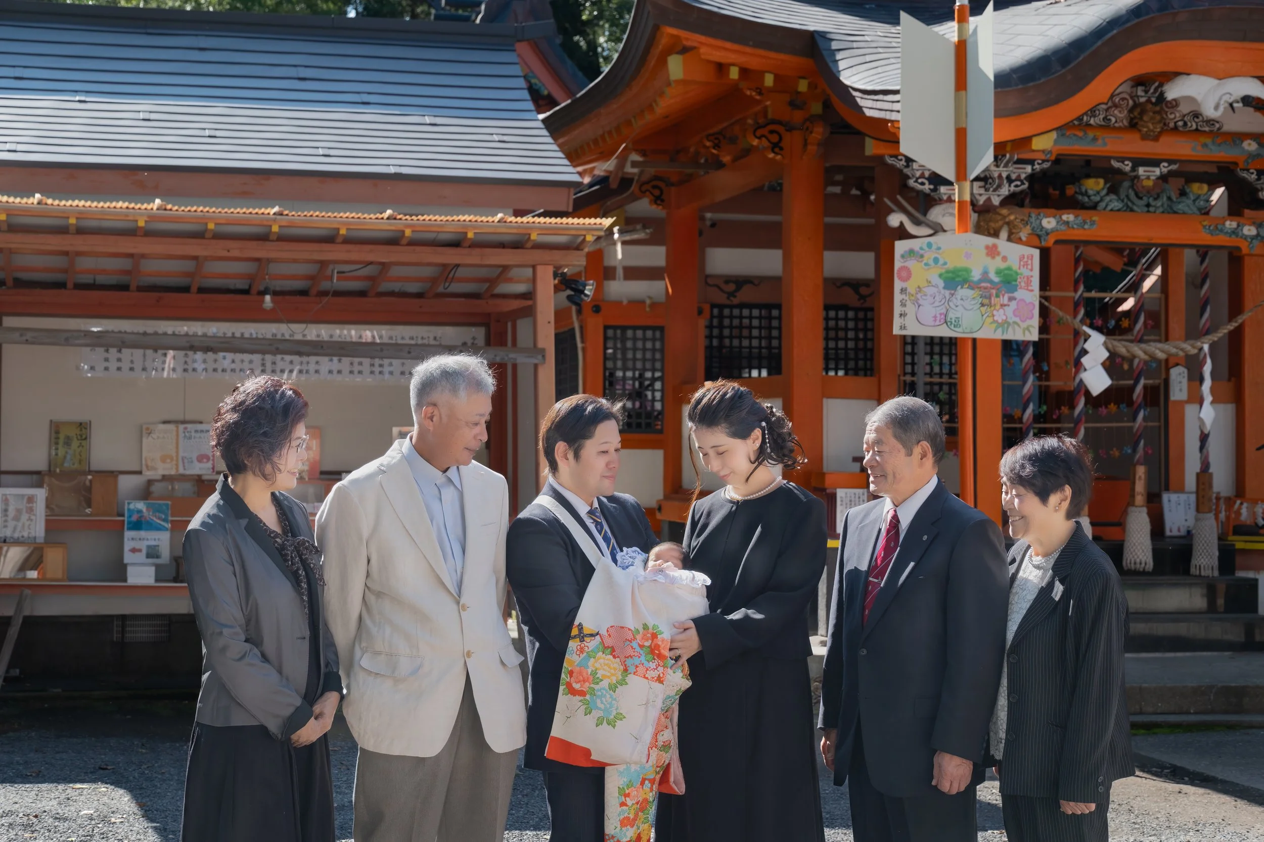 神社で赤ちゃんのお宮参りの家族の写真。家族が集まり、赤ちゃんを見守る様子。