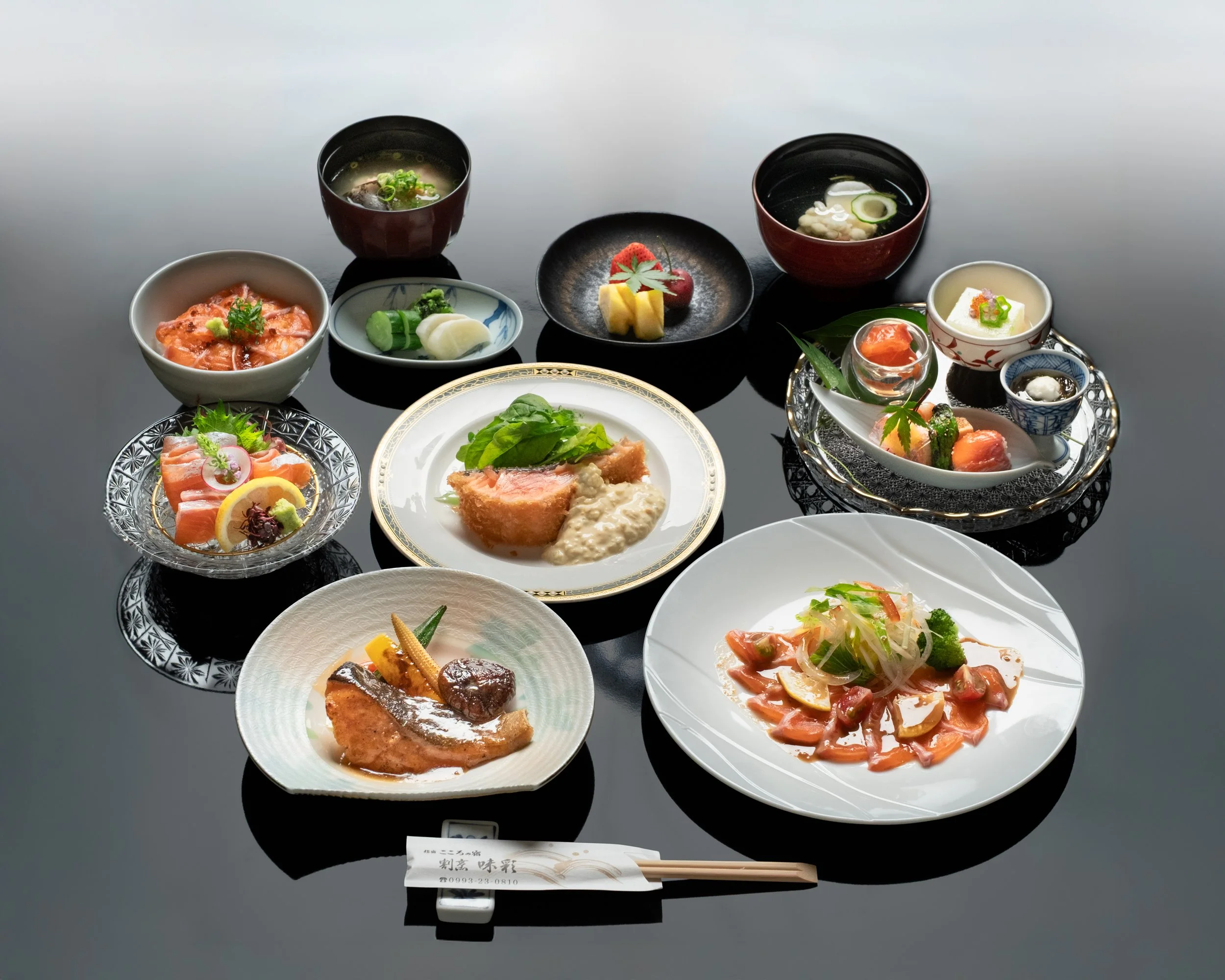 伝統的な日本料理のコース料理が黒いテーブルに並べられている。刺身、煮物、お吸い物、酢の物、果物など多彩な料理が盛り付けられている。