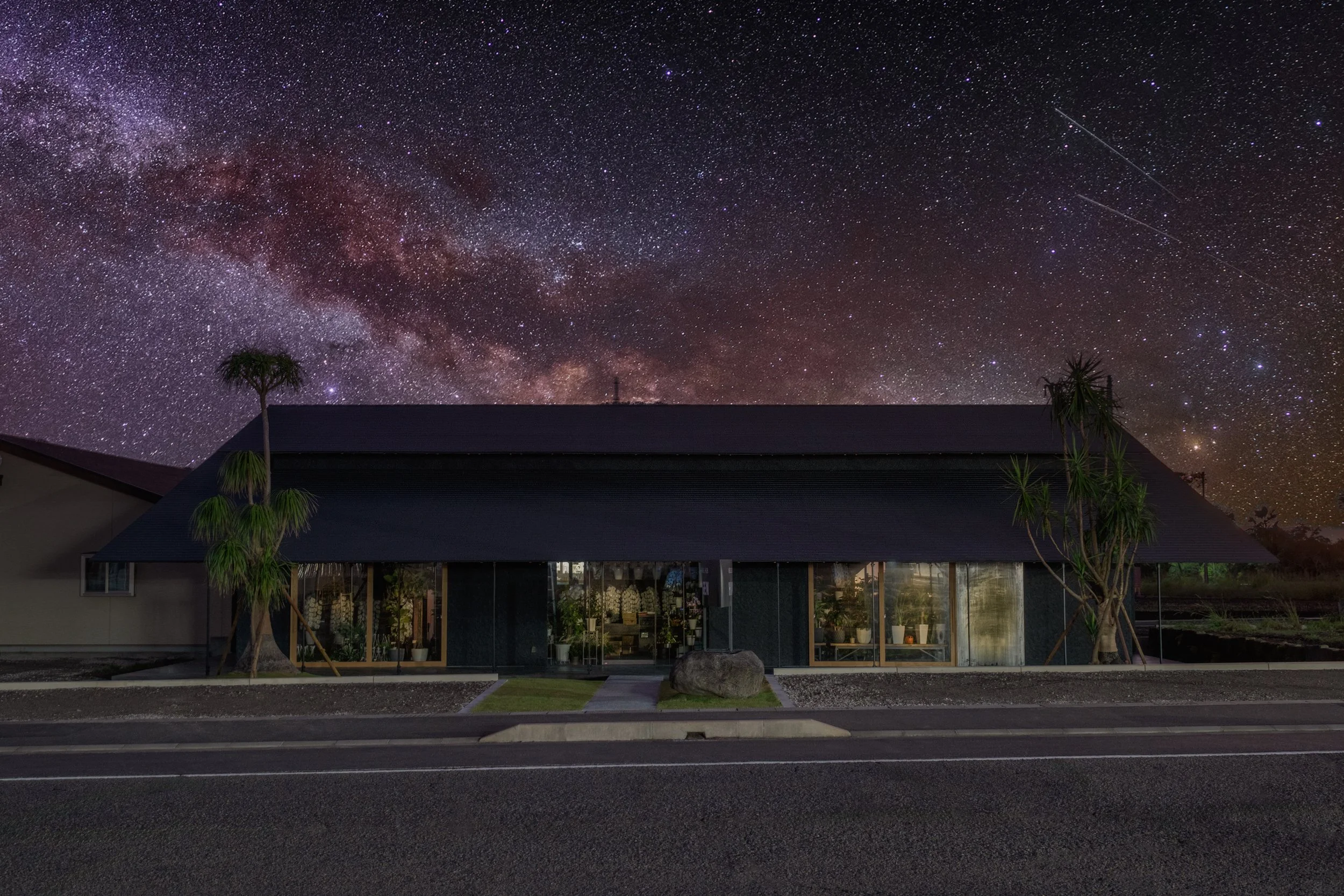 新築の花屋の前に歩道と道路があり、背景に星空と天の川が広がる夜景