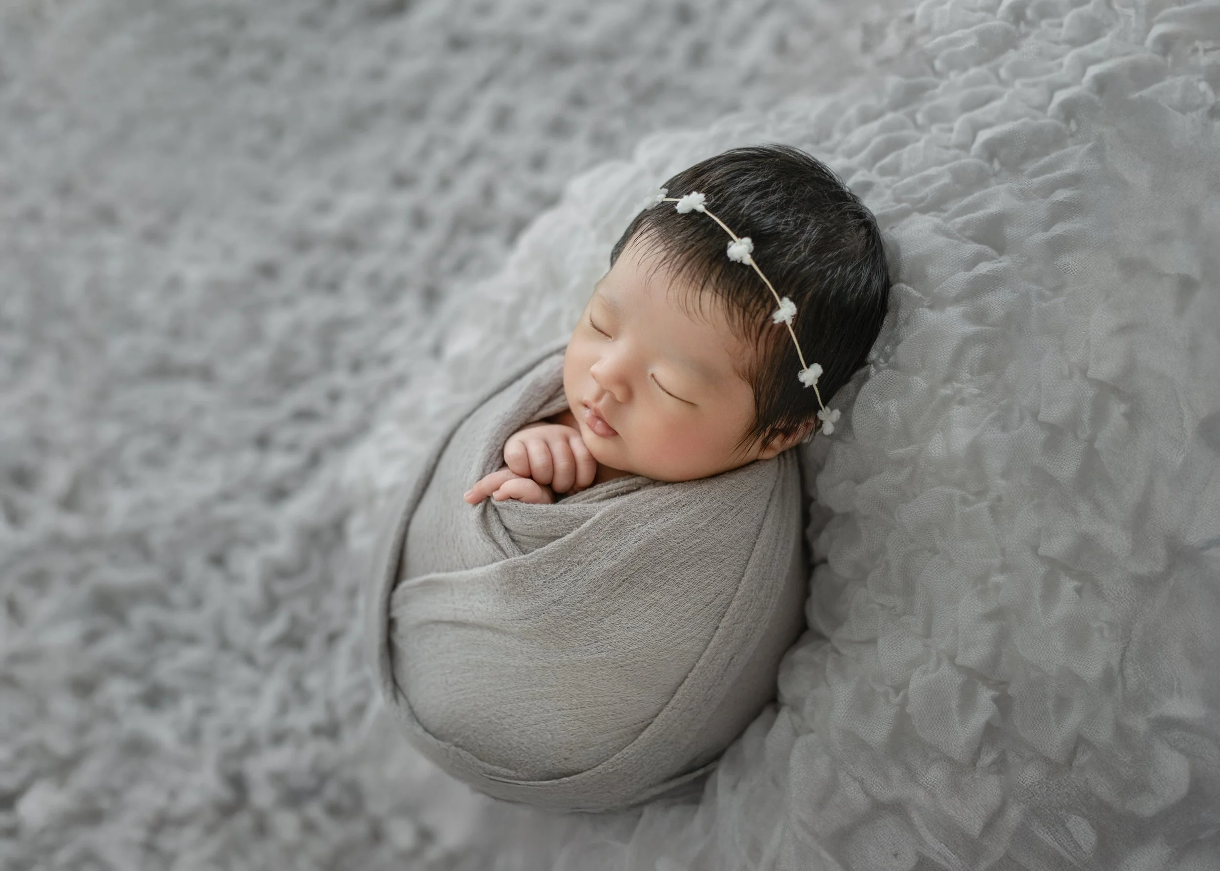 花柄のヘアバンドをつけた赤ちゃんの写真。まるまるとした顔をして、眠っている。