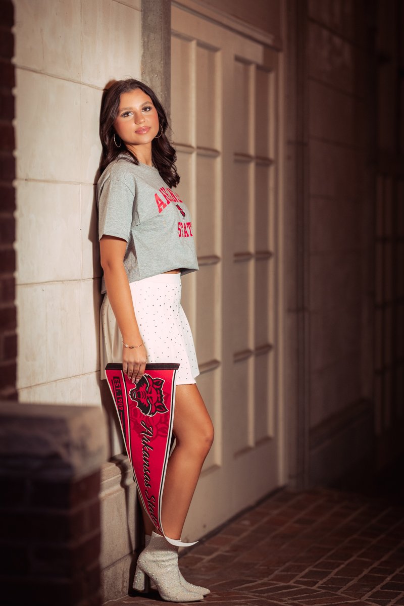 A young woman standing against a stone wall, holding a red pennant with a mascot and the words "Tulane University".