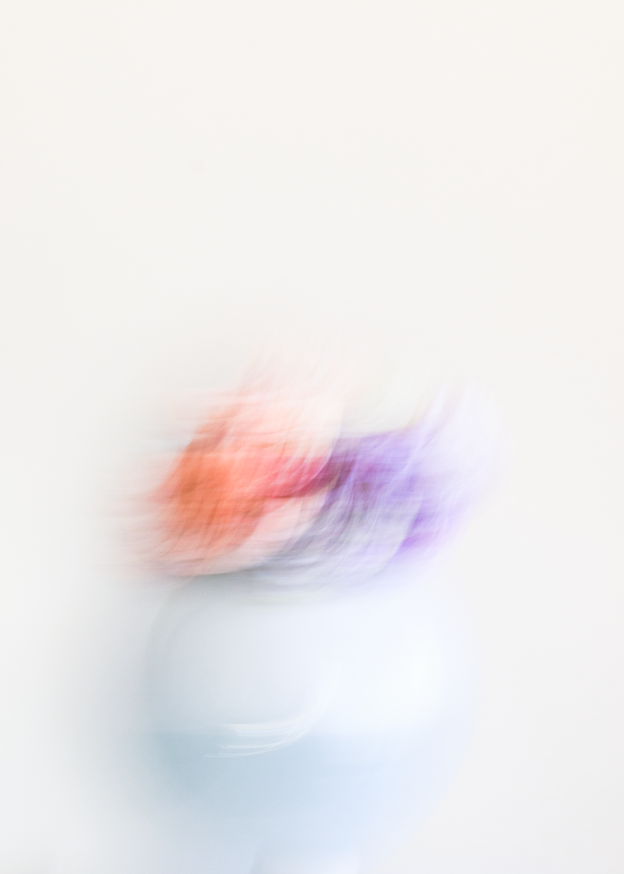 Blurred image of a white vase with colorful flowers on a plain white background.