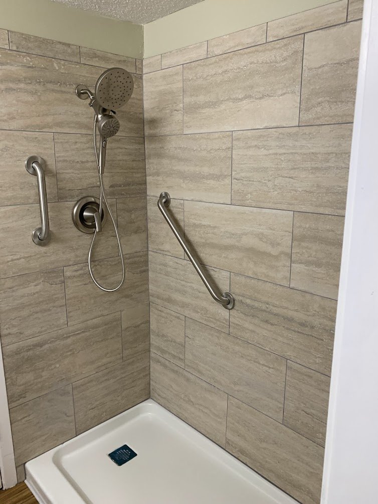 Wet-Room Base: Low-threshold shower pan set flush for wheelchair roll-in access.