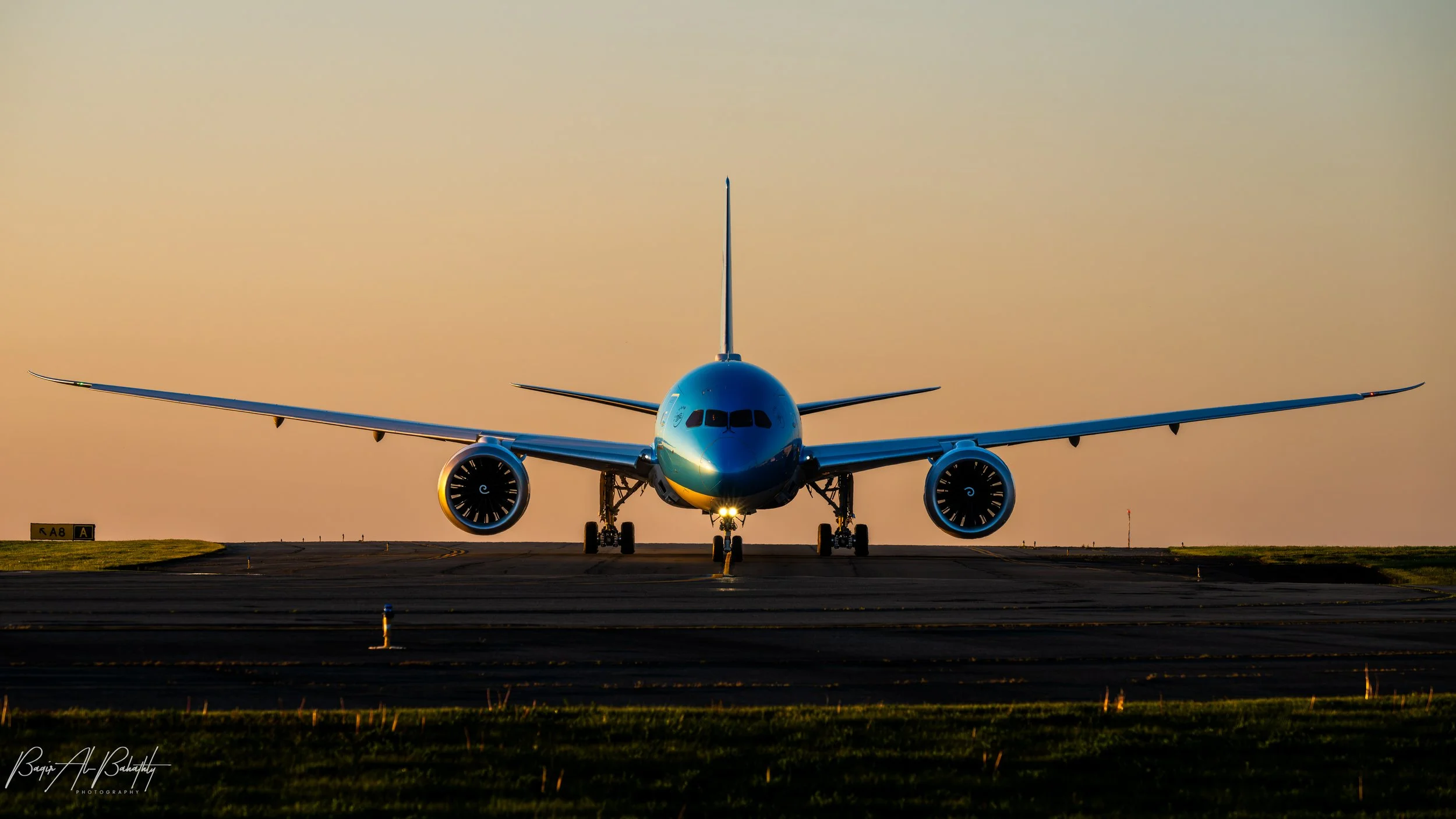 Front view of a commercial airplane on the runway during sunset with the wings extended and engines visible.