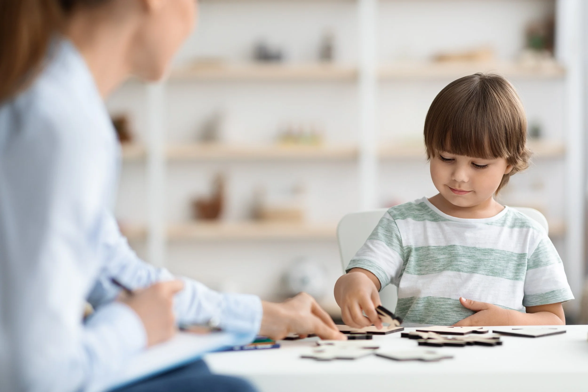 A young boy playing a matching card game with an adult at a white table in a bright, cozy room.