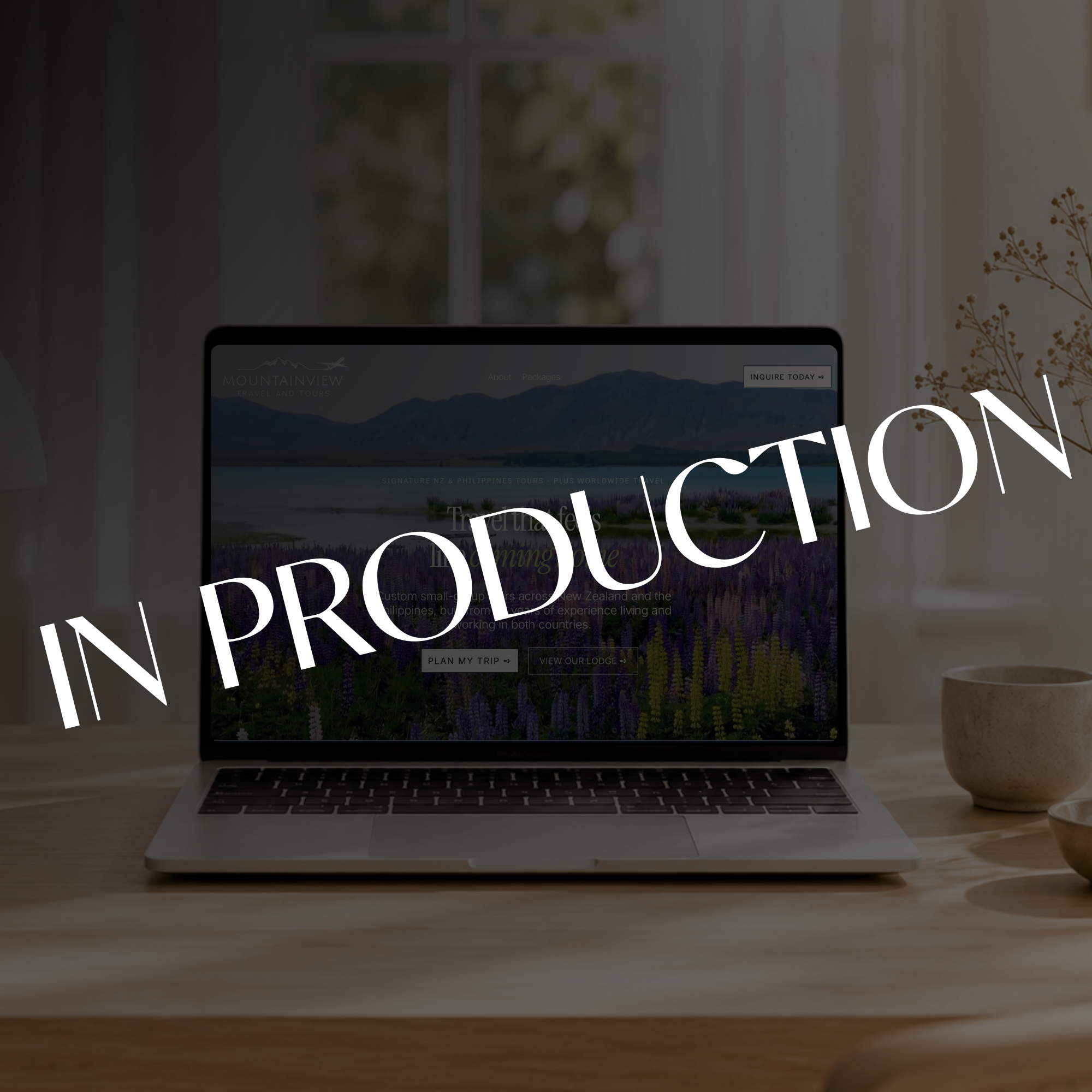 Laptop displaying a Mountainview Travel and Tours website with a New Zealand mountain and lupine field, overlaid with large “WORK IN PRODUCTION” text.