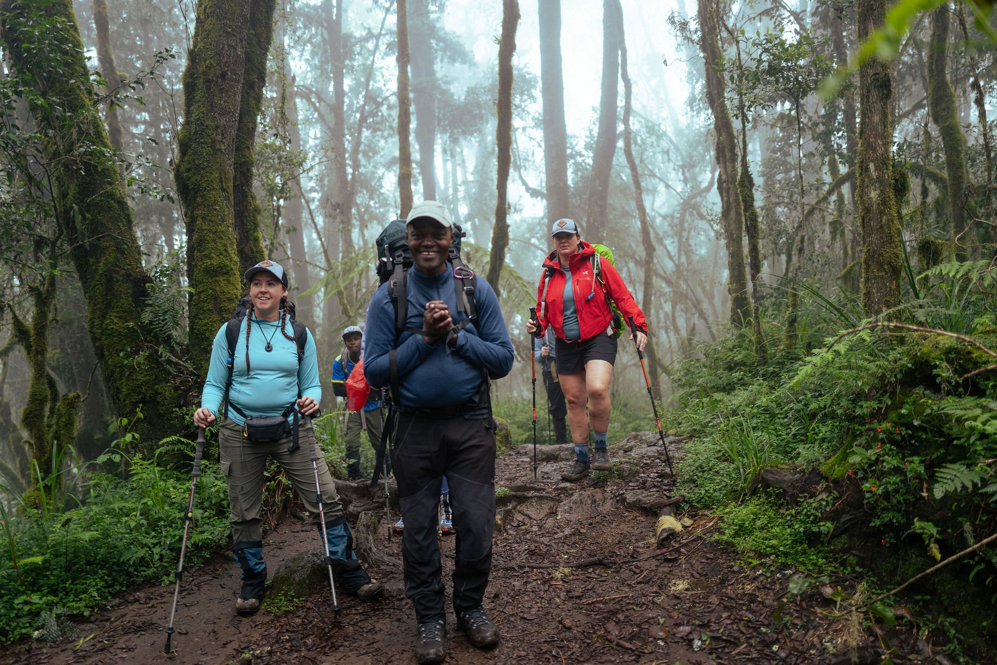 Group of hikers walking through a foggy, lush green forest on a muddy trail.