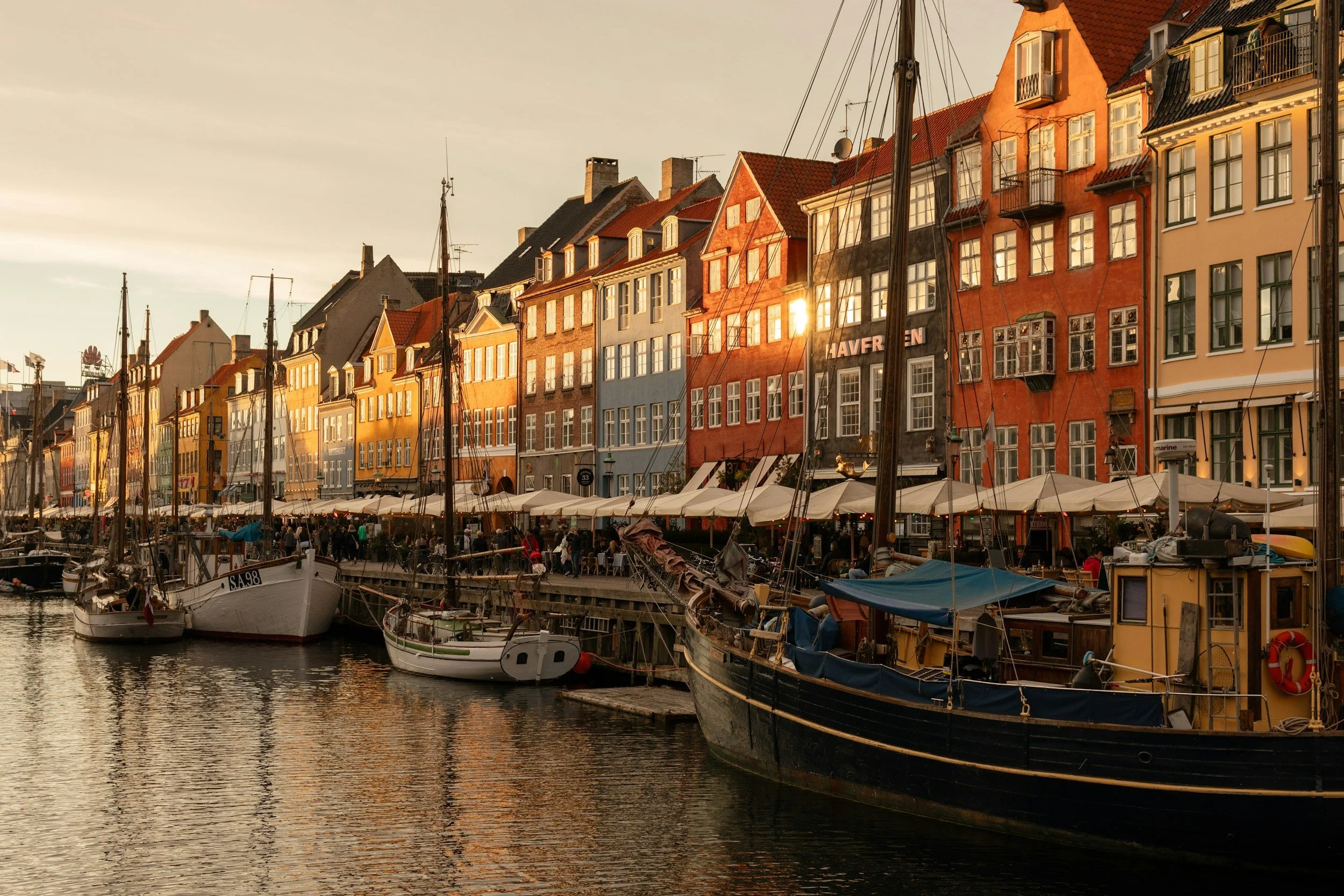 Colorful row of buildings along a waterfront with boats docked in the harbor at sunset.
