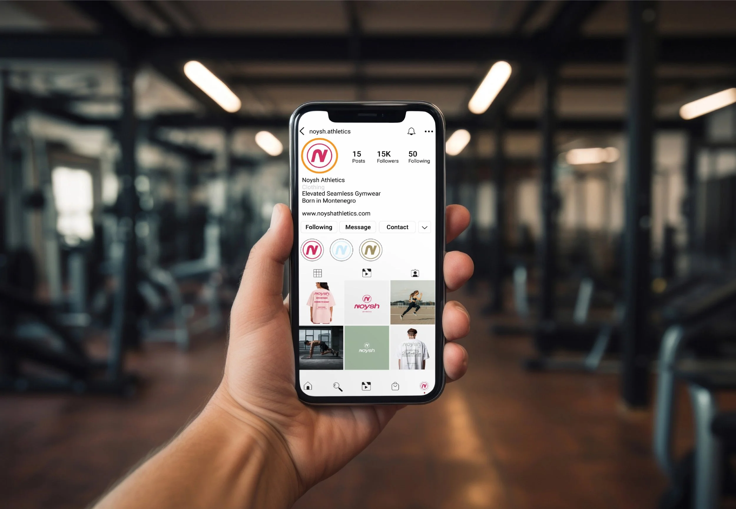 A person holding a smartphone displaying the Instagram profile of Noysh Athletics. The profile includes images of athletic clothing and workout photos, with a gym in the background.
