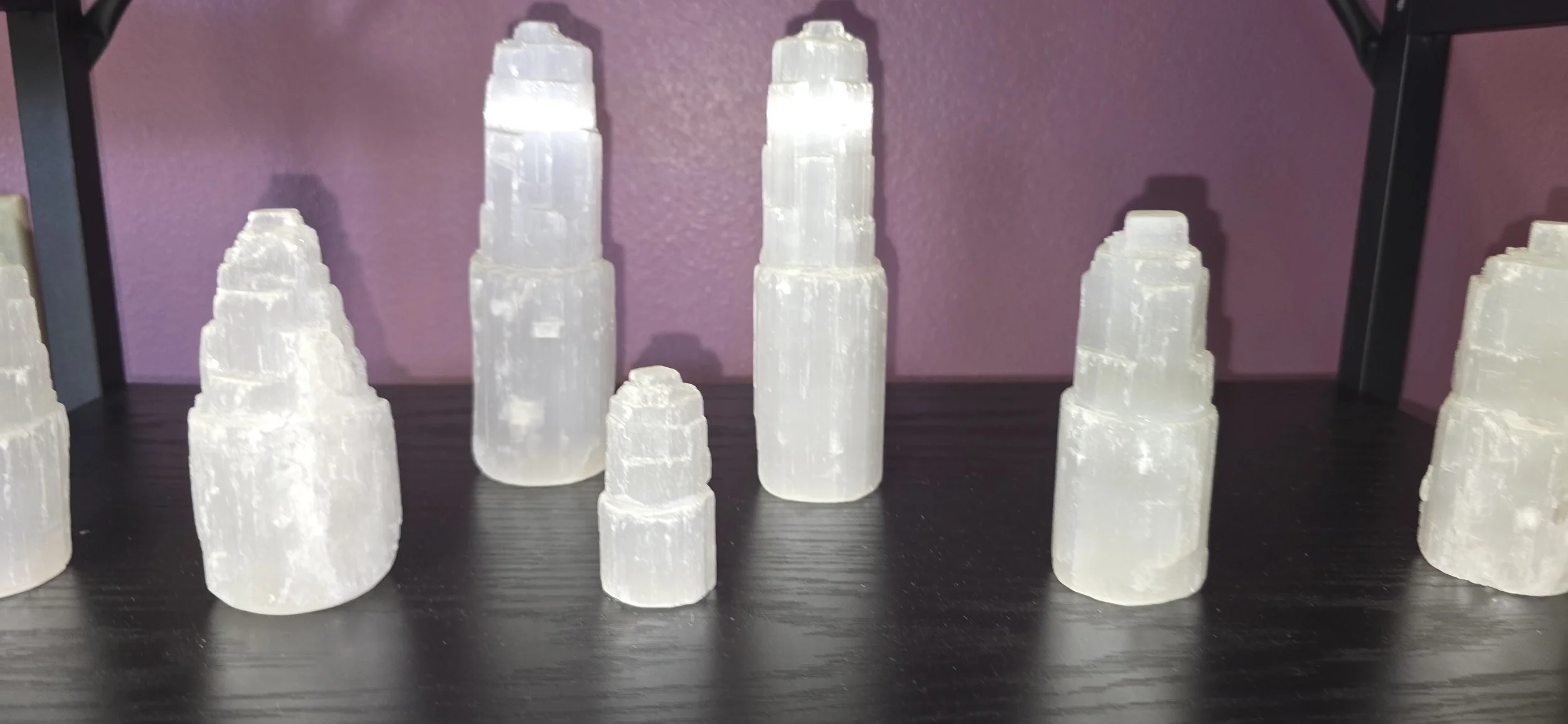 Collection of selenite towers on a black surface with a purple wall background.