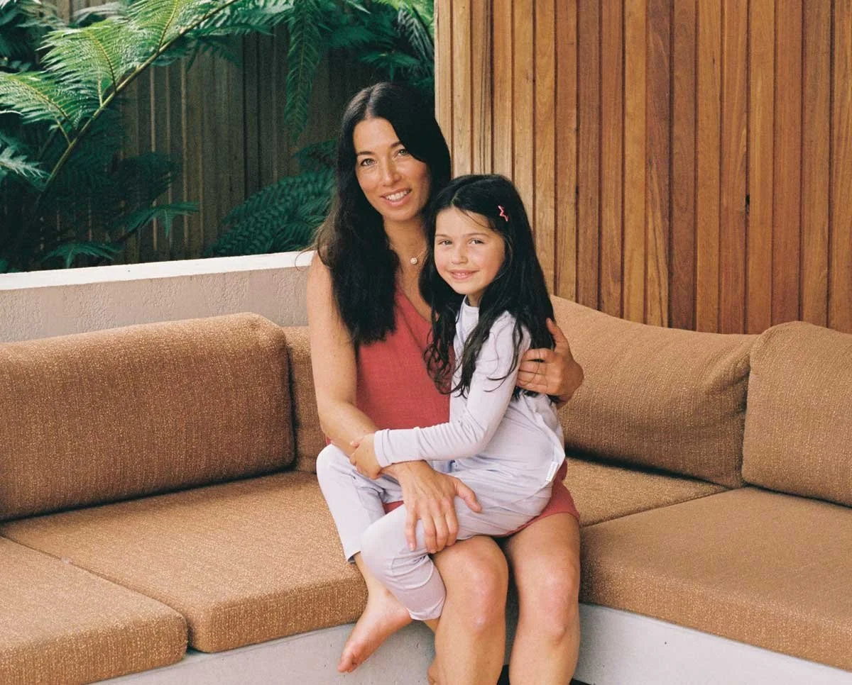 A woman and a girl sitting together on a brown sectional sofa, smiling for the camera.