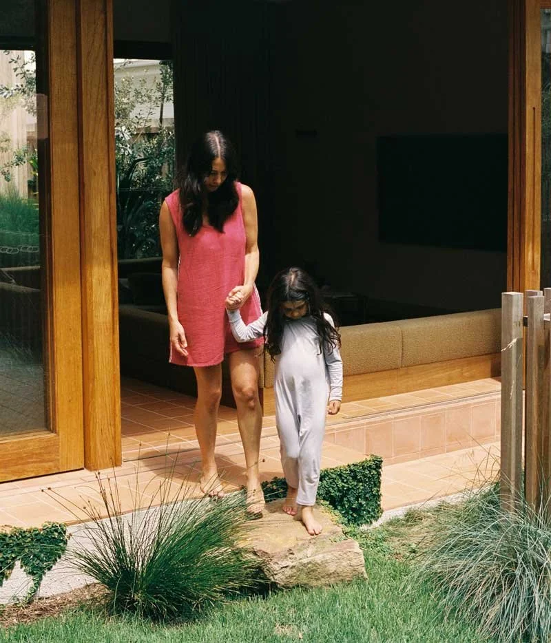 A woman and young girl walking outside on a stone path near a house.
