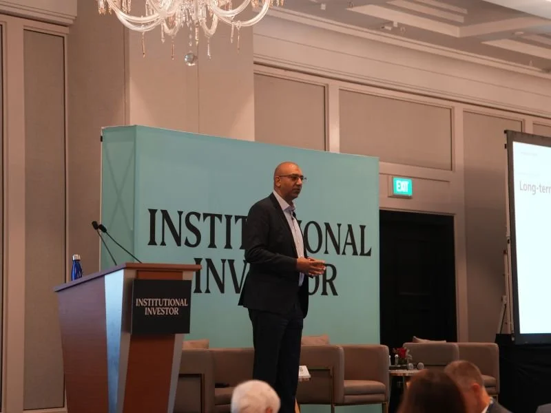Man in suit giving a presentation at the Institutional Investor conference in a hotel ballroom.