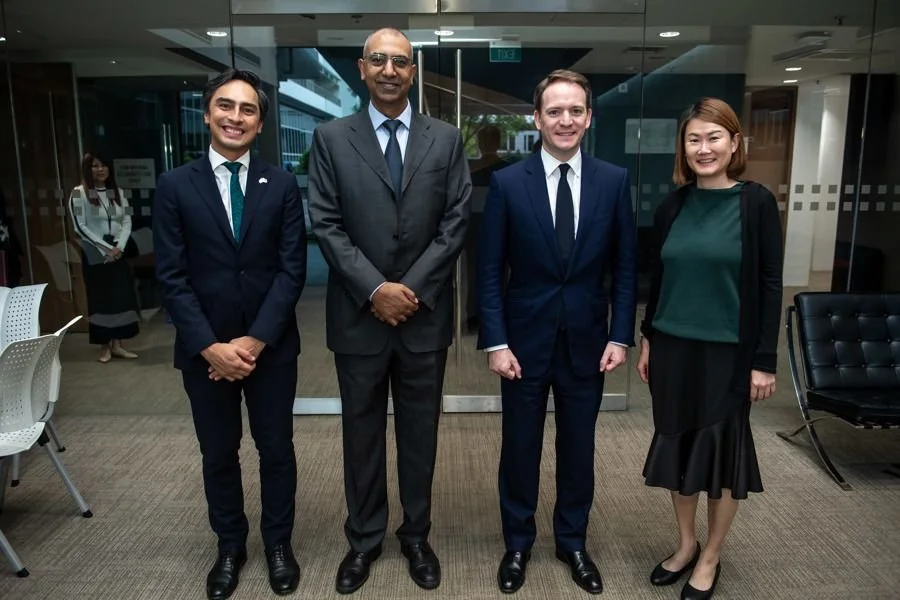 Four professionally dressed individuals standing in an office lobby, smiling at the camera.
