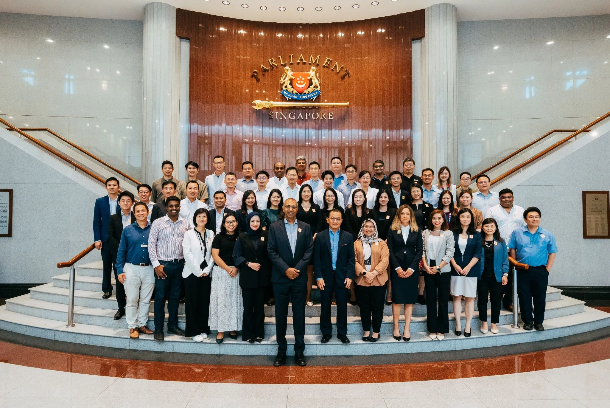 Group of people standing in front of the Parliament Singapore logo inside the building.