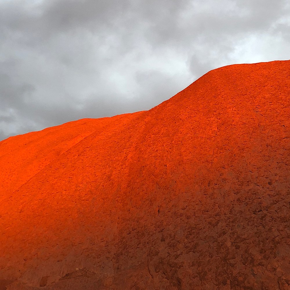 Red sandstone formation with a curved surface beneath a cloudy sky.