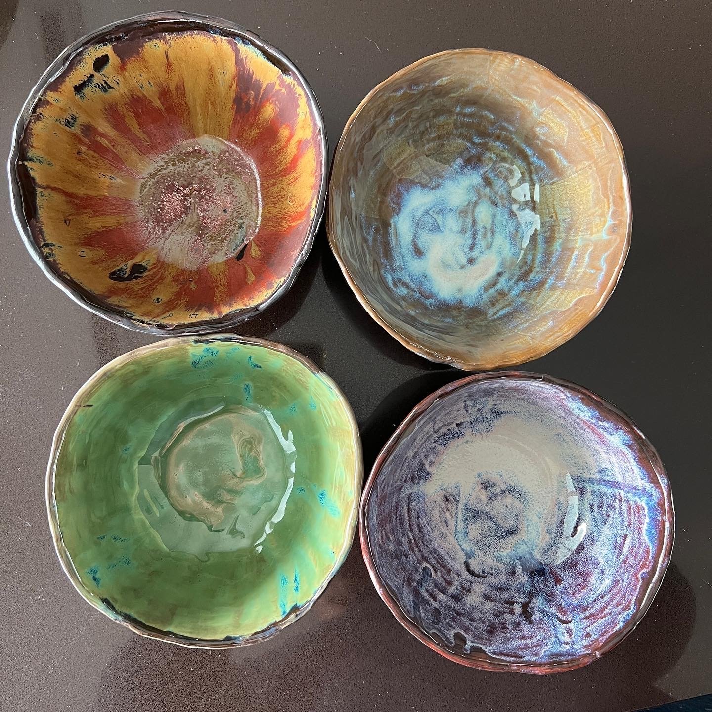 Four colorful, handcrafted ceramic bowls with abstract designs, arranged on a dark surface.