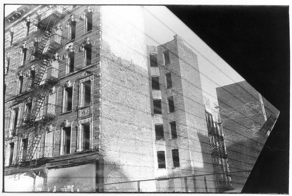 Black and white photo of a multi-story building under construction with a visible scaffolding and adjacent older brick building.