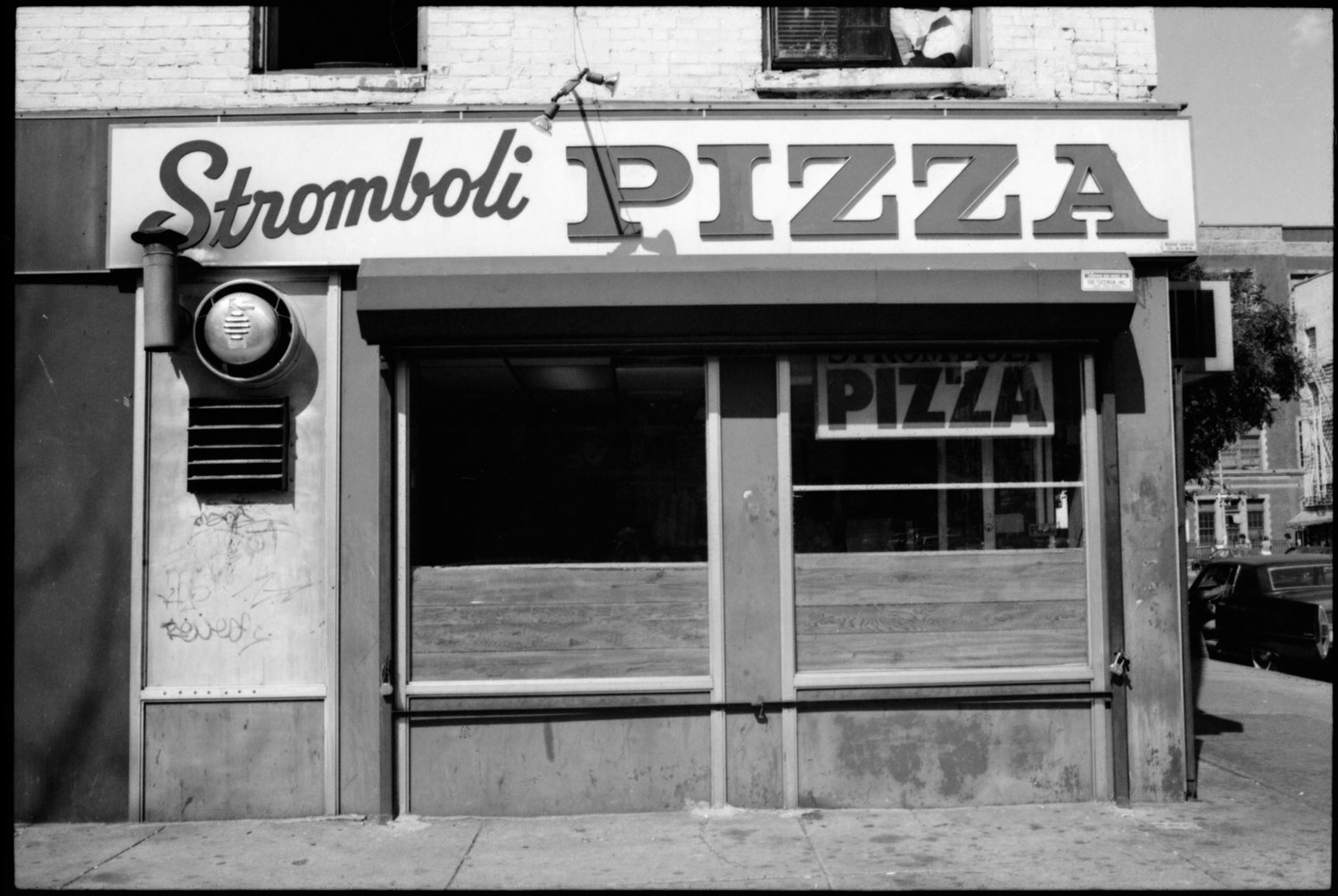 Black and white photo of a vacant storefront with a sign that reads 'Stromboli PIZZA'.