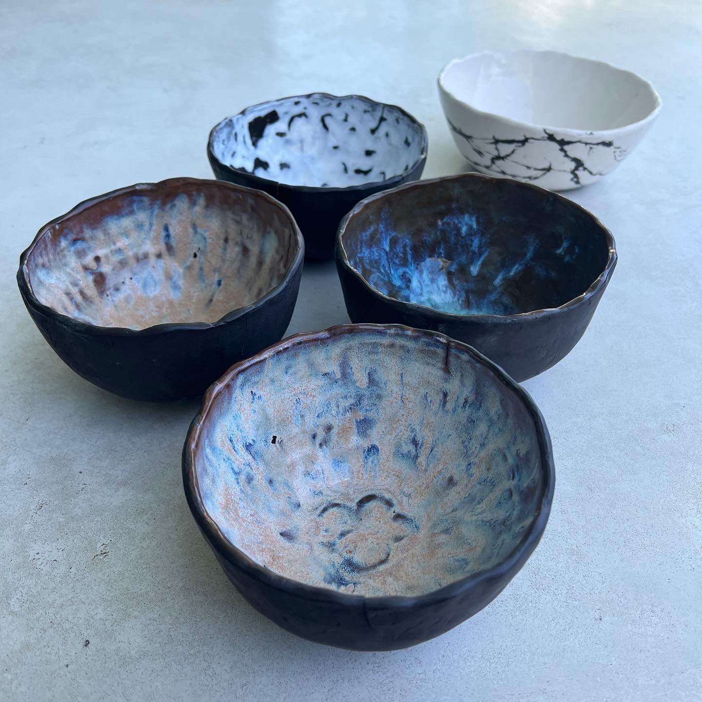 Seven ceramic bowls with different black and white or blue and tan glaze patterns on a light surface.
