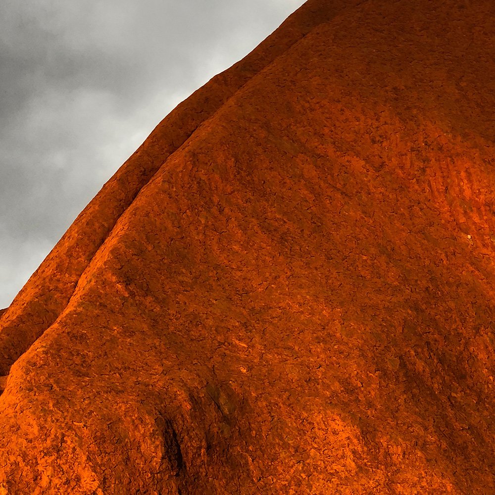 Close-up of a large, rust-colored, textured rock formation against a cloudy sky.