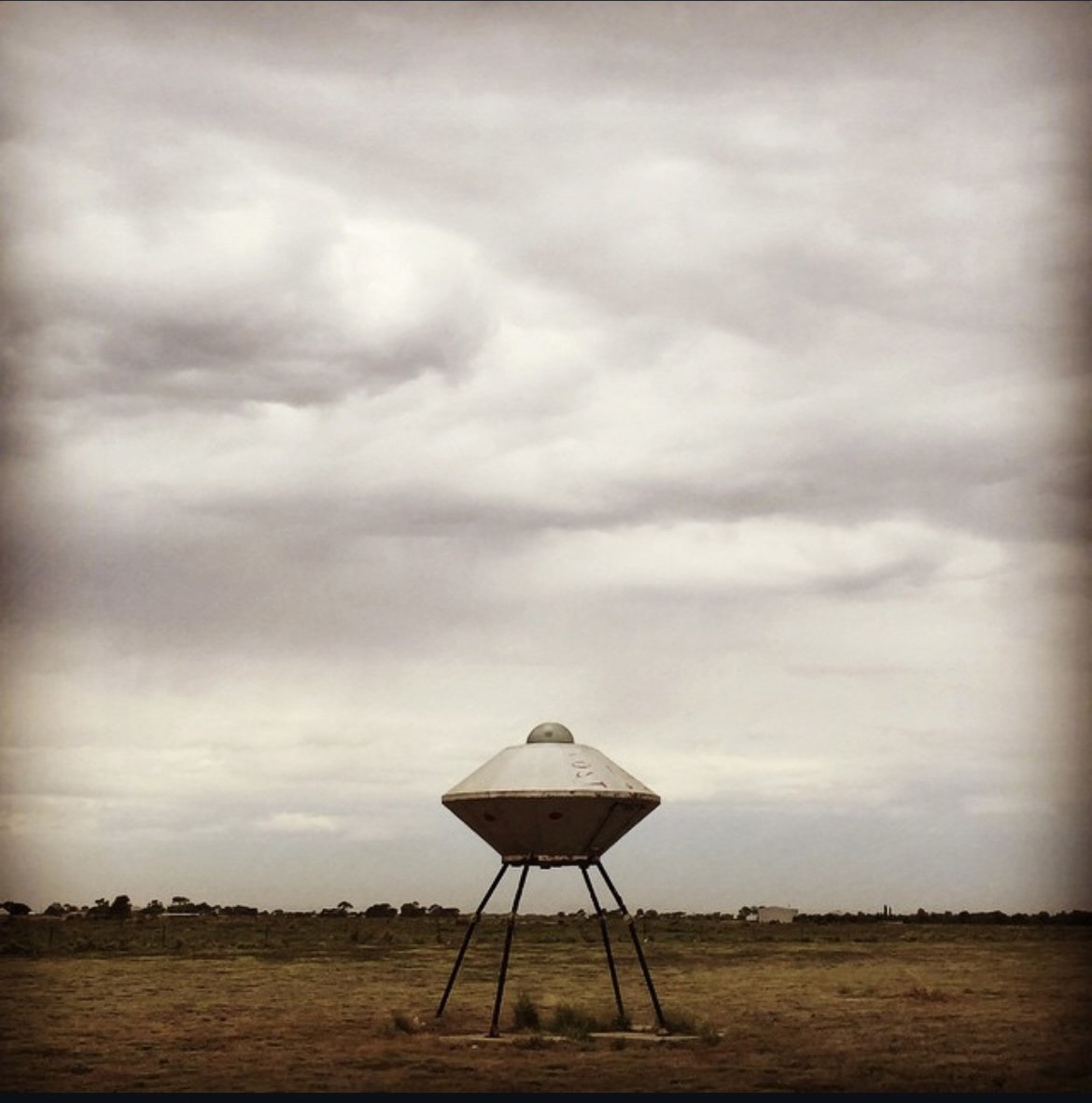 A UFO-shaped structure with three legs standing on a flat, open landscape under a cloudy sky.