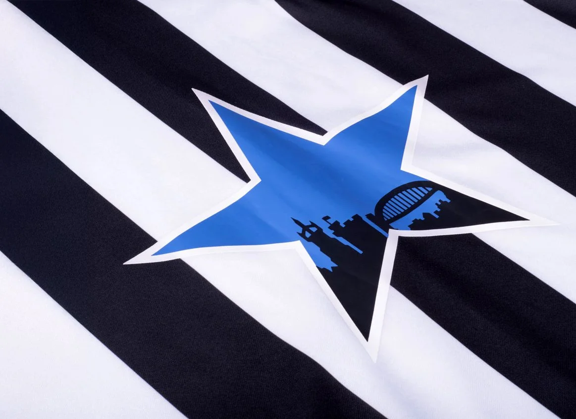 A sports jersey with black and white horizontal stripes and a blue star logo in the center. The logo features city skyline silhouettes inside the star.