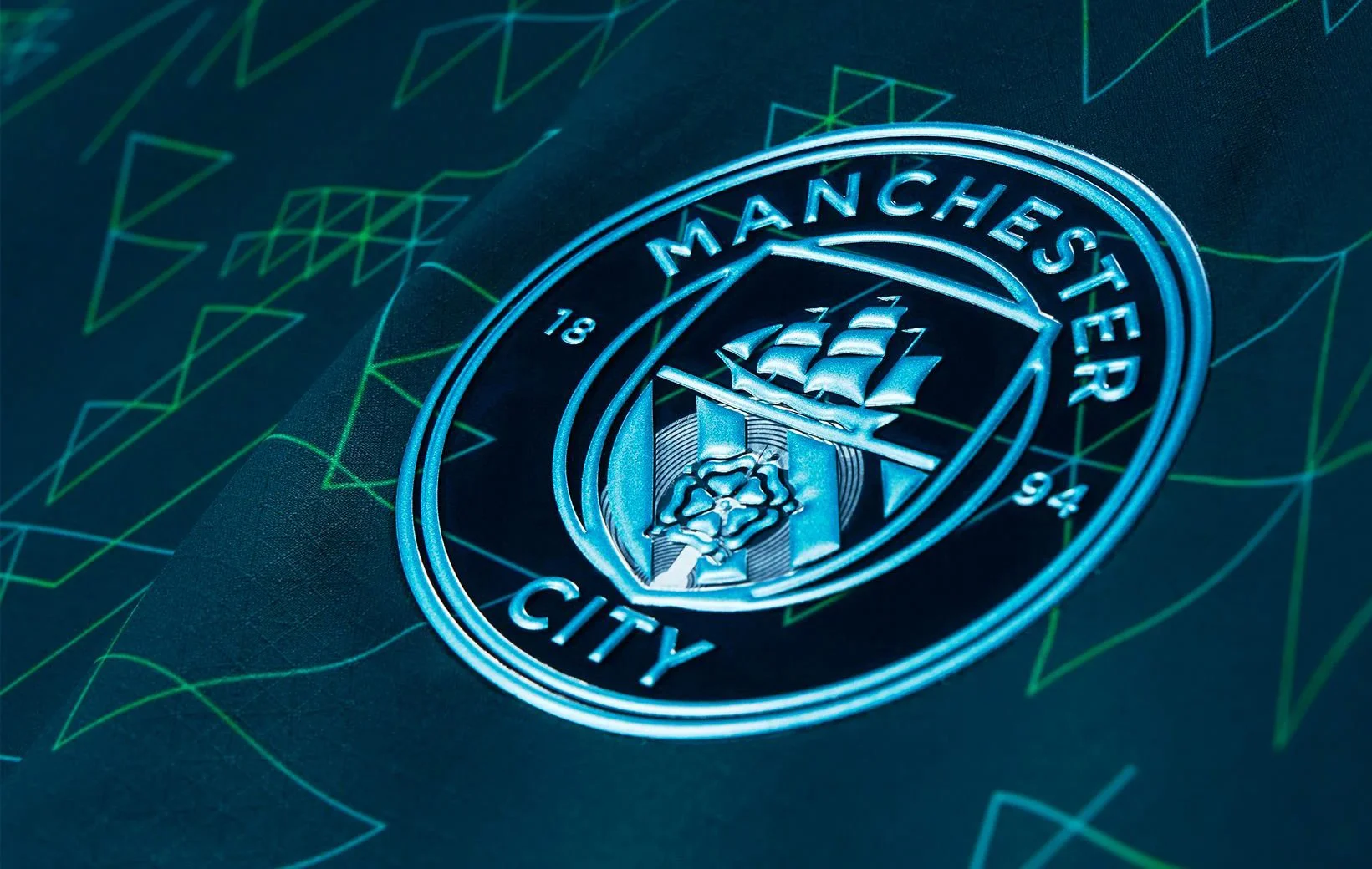 Close-up of Manchester City football club emblem illuminated in blue with a background of digital line graphs in green and blue.