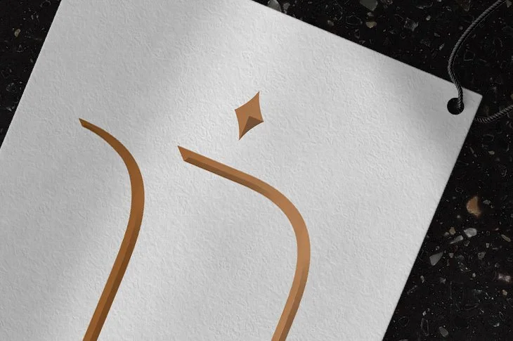 Close-up of a white textured card with a brown coffee cup illustration and a small star shape, on a black surface with a string attached.