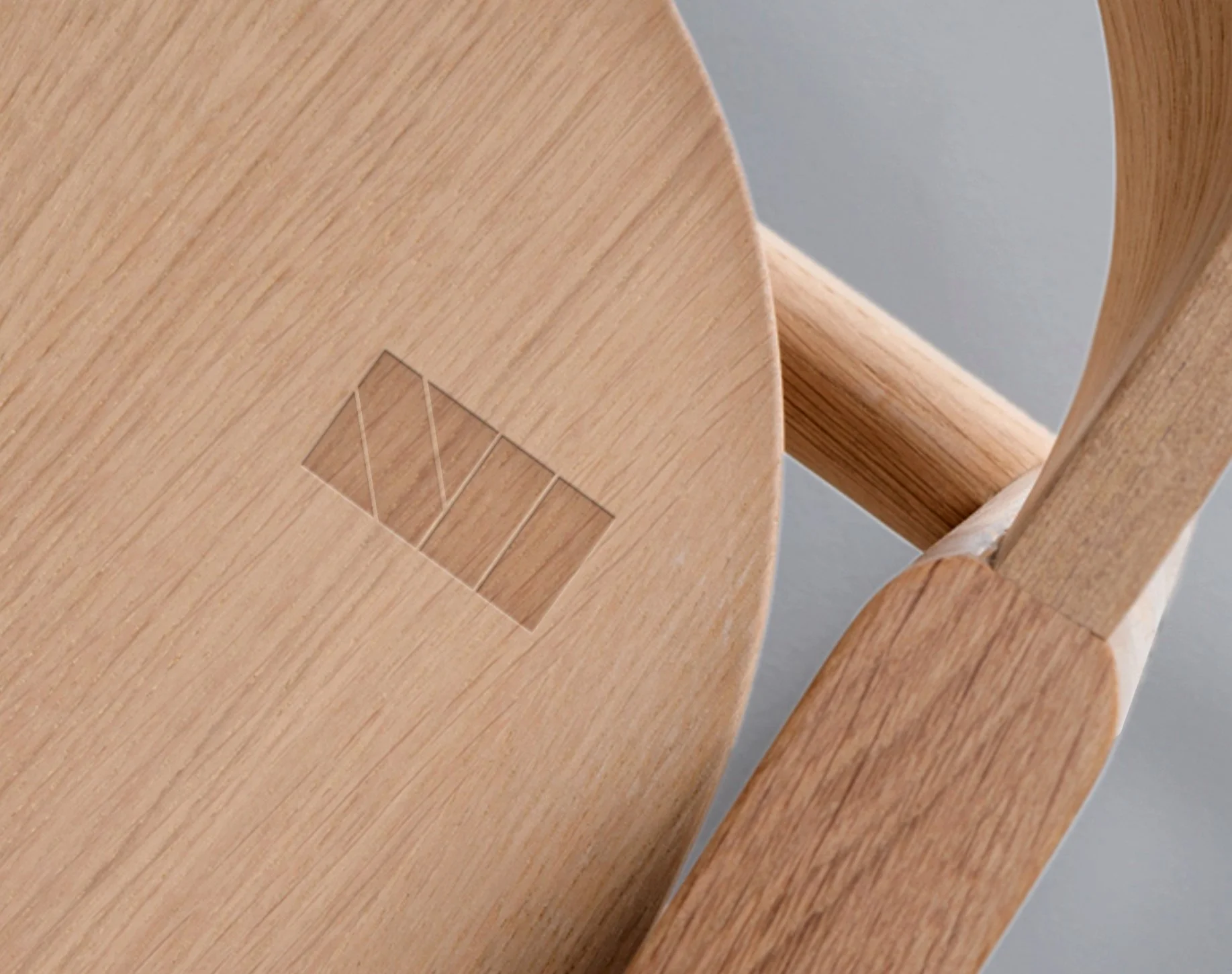 Close-up of a wooden chair leg and a section of the seat with a small, transparent logo or design embedded in the wood.