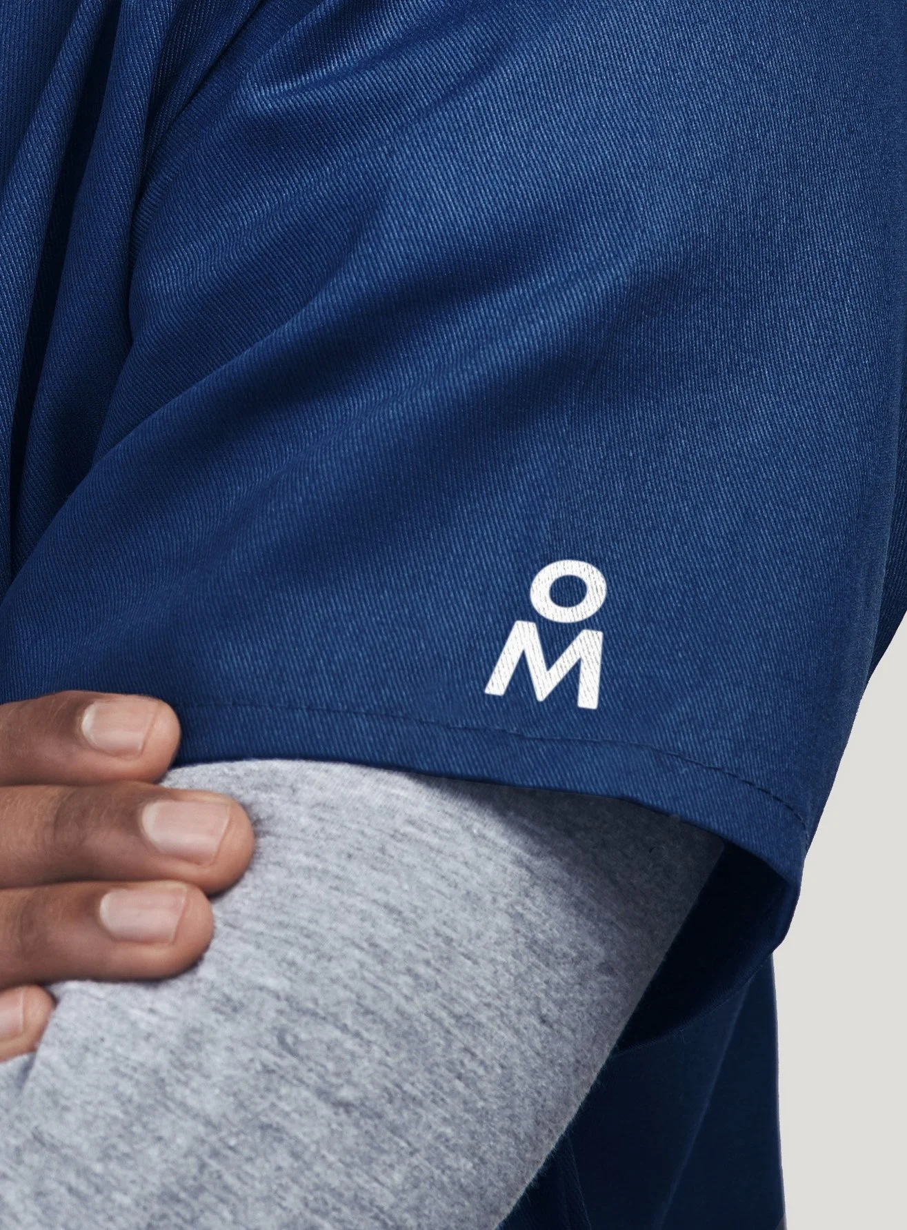 Close-up of a person wearing a blue garment with a white logo, and a hand resting on a gray fabric.