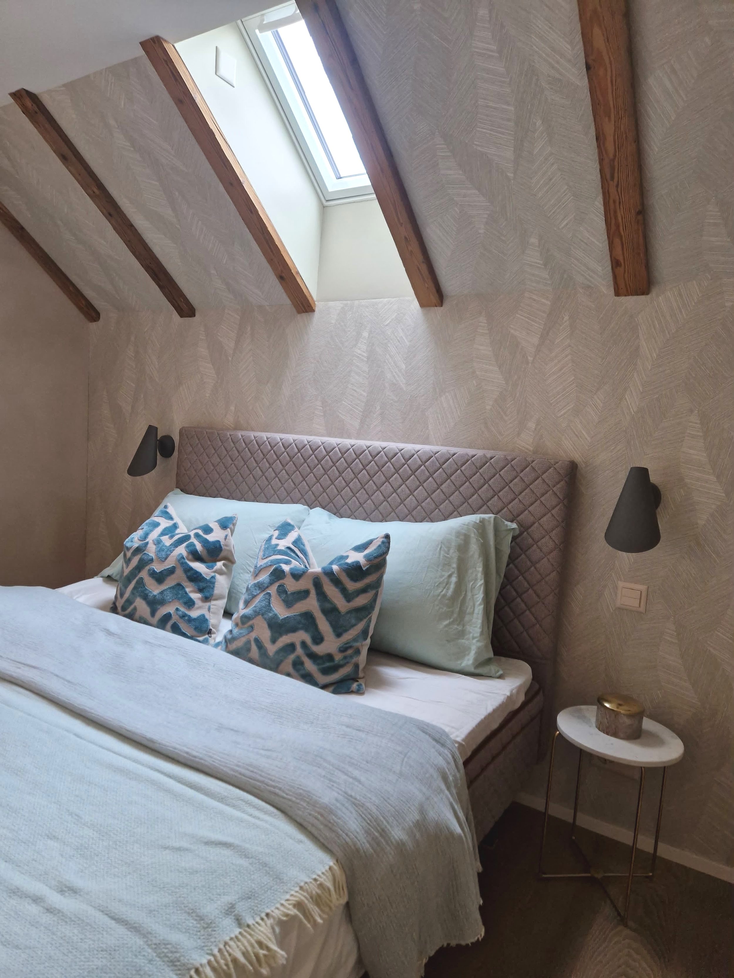 Schlafzimmer mit Dachfenster, beige bedingt mit Kissen, Wandlampen und Nachttisch
