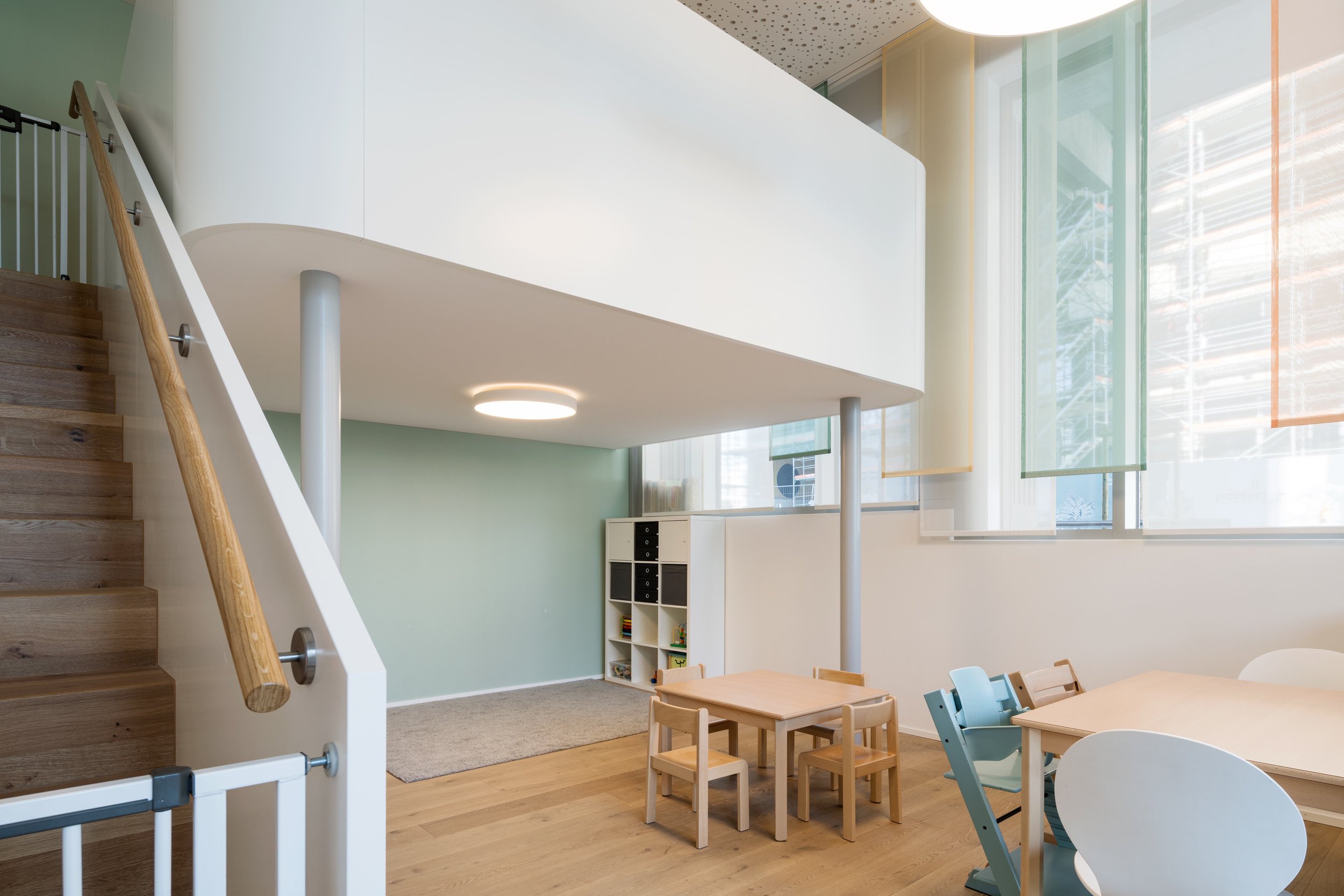 Innenraum eines modernen Spiel- oder Lernraums mit Treppe, Kinderstühlen, Tischen und bunten Fensterläden