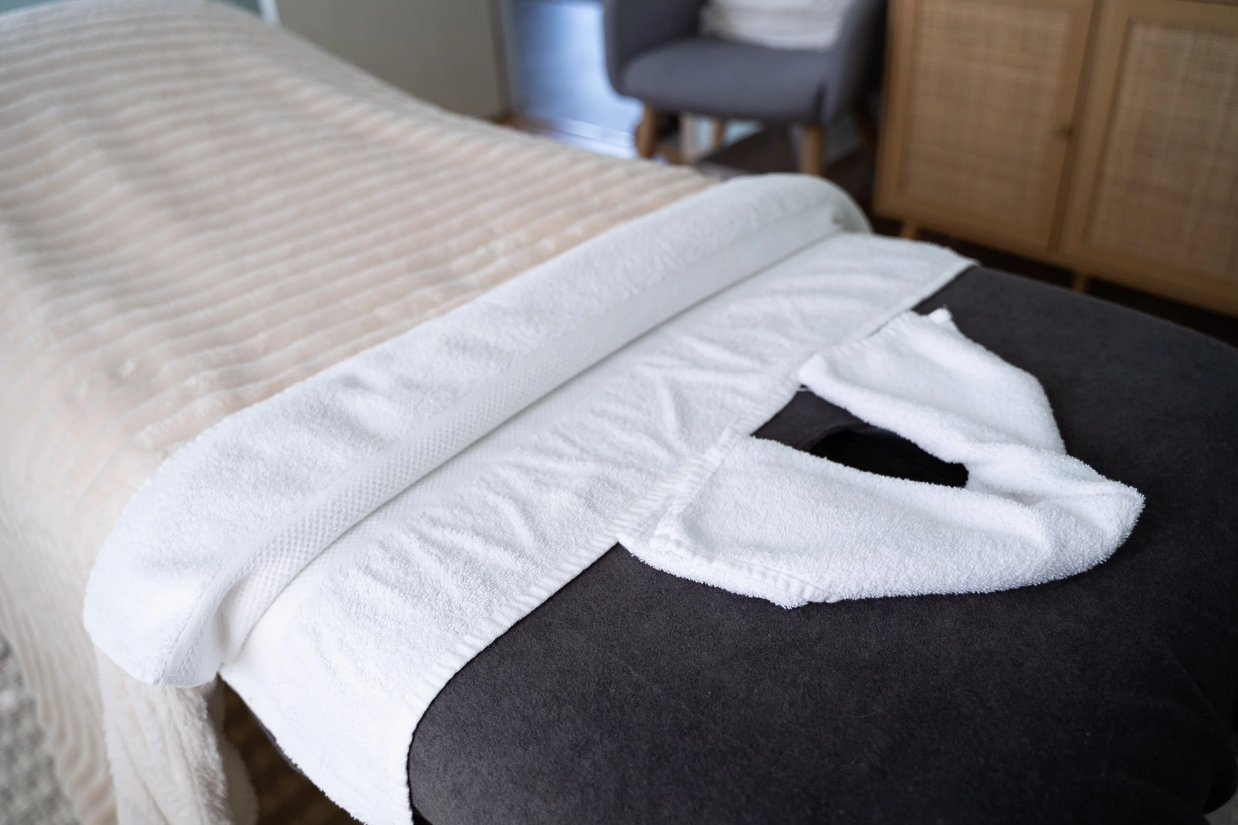 Close-up of a bed with a beige and white textured blanket, a white towel, and a black sheet underneath, in a bedroom setting.
