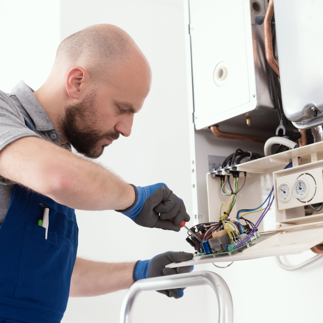 A technician wearing gloves working on electrical wiring inside a wall-mounted panel.