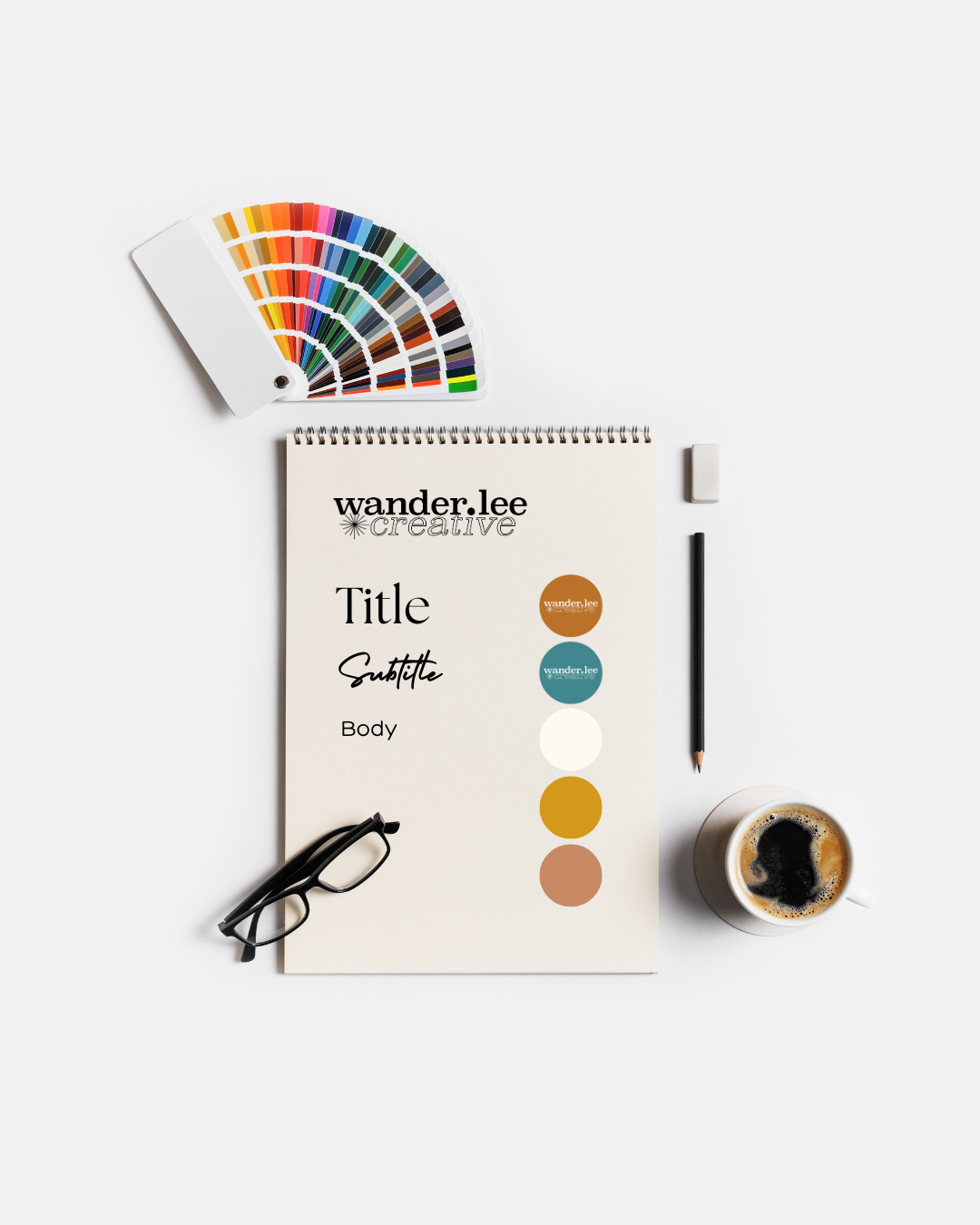 Flat lay of a creative branding or design workspace, including a color palette fan deck, glasses, a notepad with design placeholder text, a pencil, a cup of coffee, and an eraser on a white background.