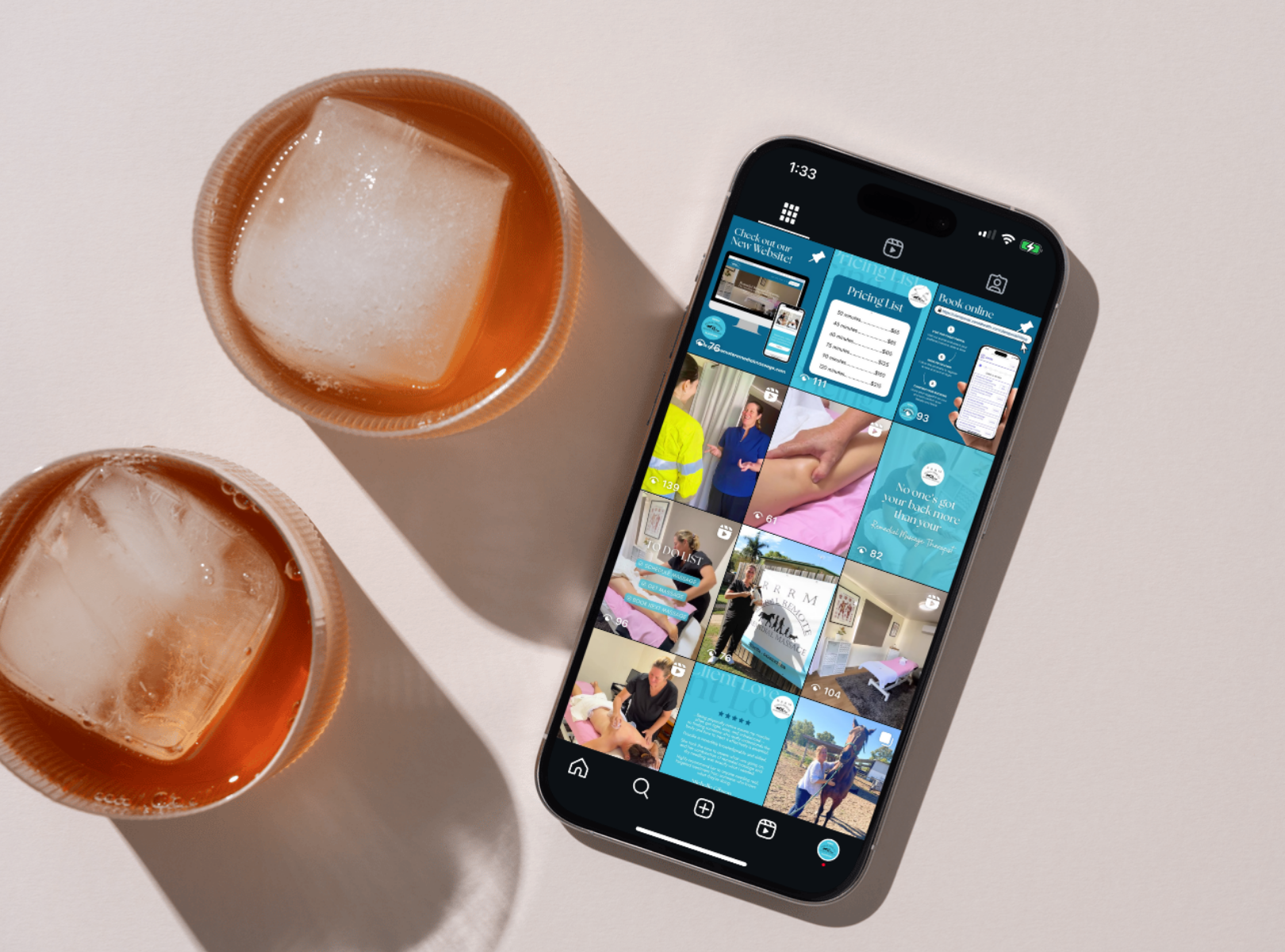 Two glasses of iced tea with large ice cubes and an iPhone displaying a social media app on a white surface.