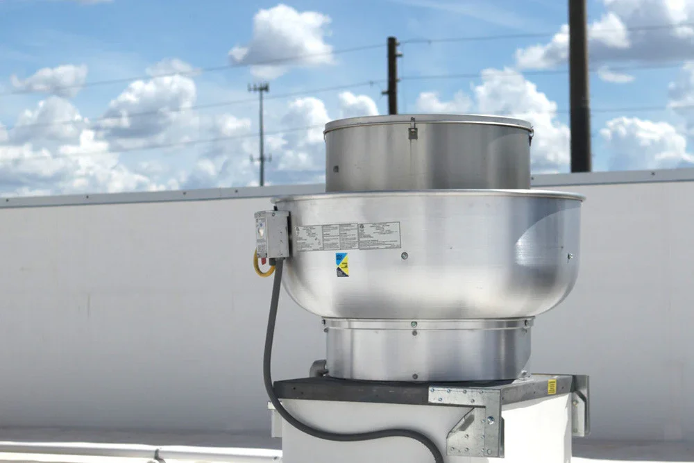 An industrial air conditioning or ventilation unit mounted on a rooftop, with a blue sky and white clouds in the background.