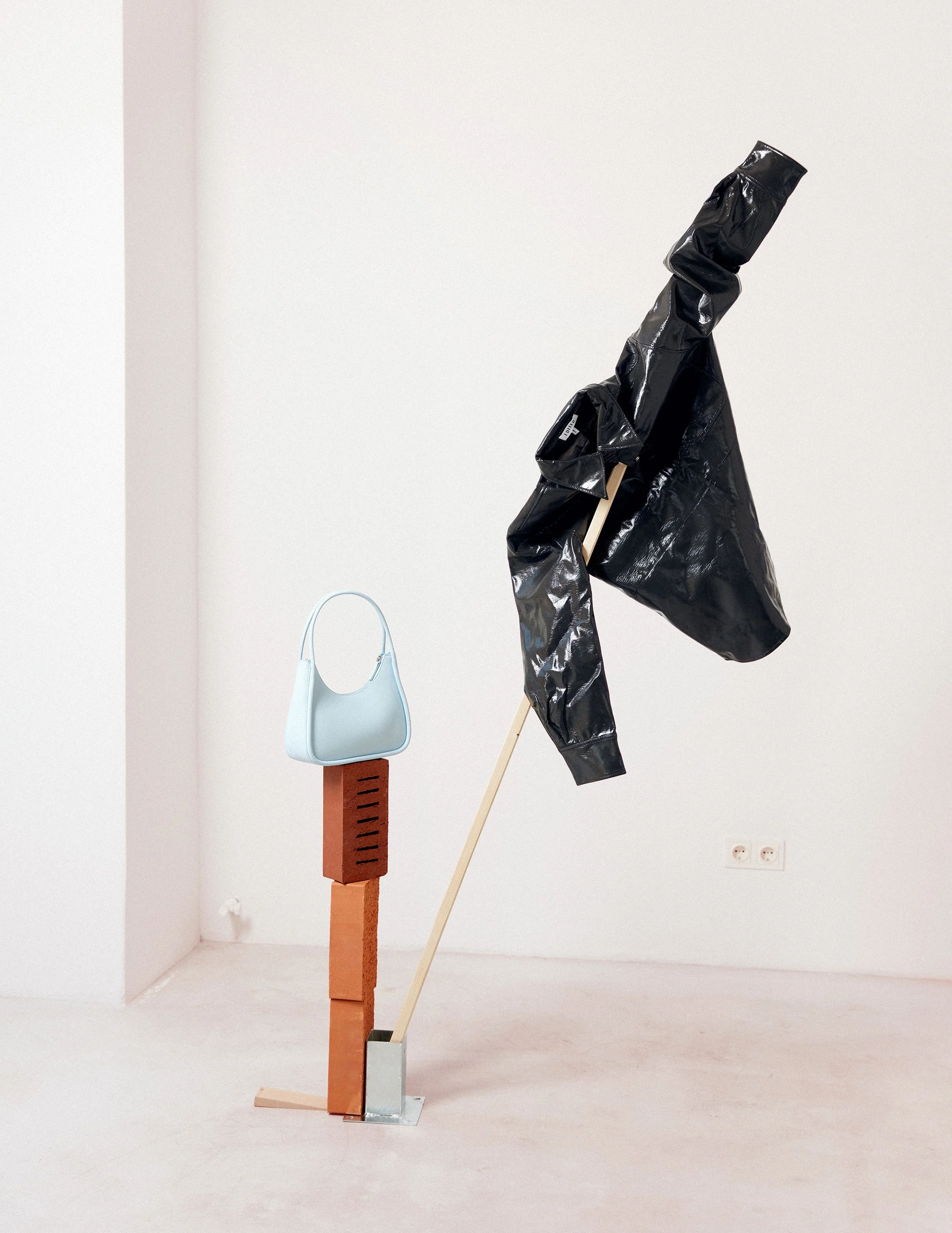 Still life editorial with glossy black jacket and light blue handbag on brick pedestal, art direction and styling by Steffi Bühlmaier, photography by Jessica Grossmann for Heyday Magazine, 2022