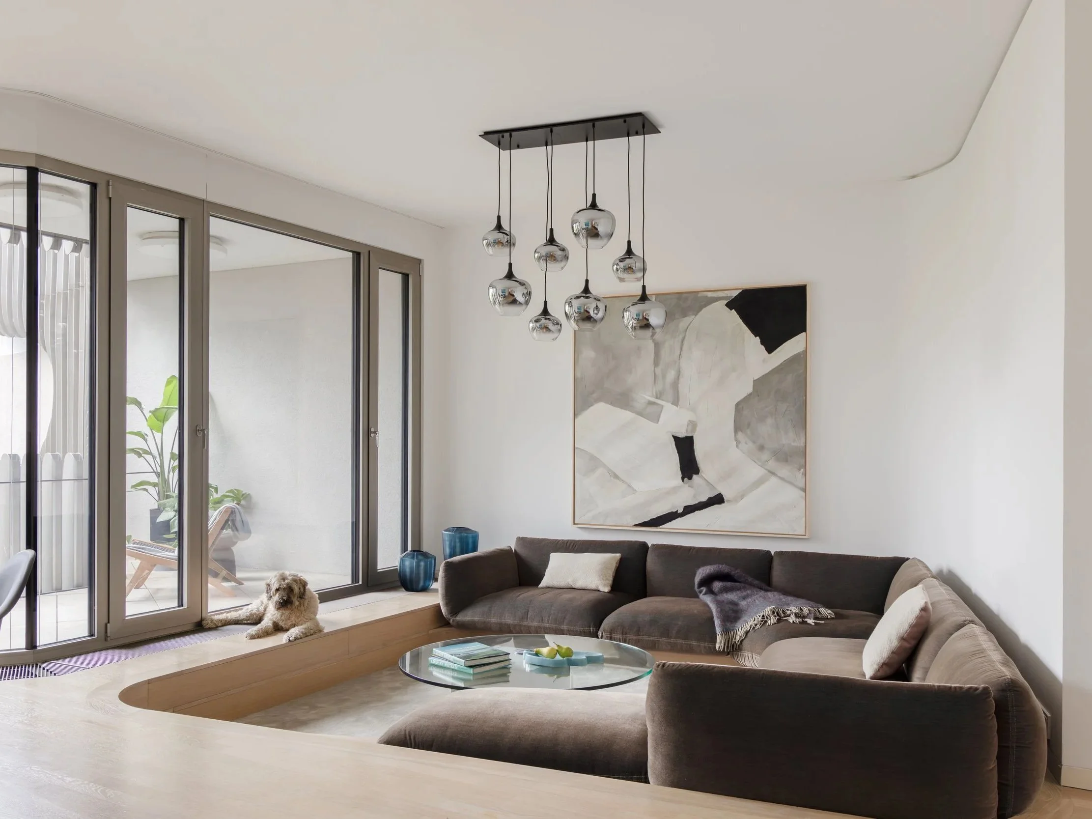 Modern living room with brown sectional sofa, glass coffee table and large abstract painting, apartment in Berlin Mitte, home staging and interior styling by Steffi Bühlmaier, photography by Jordana Schramm, 2025