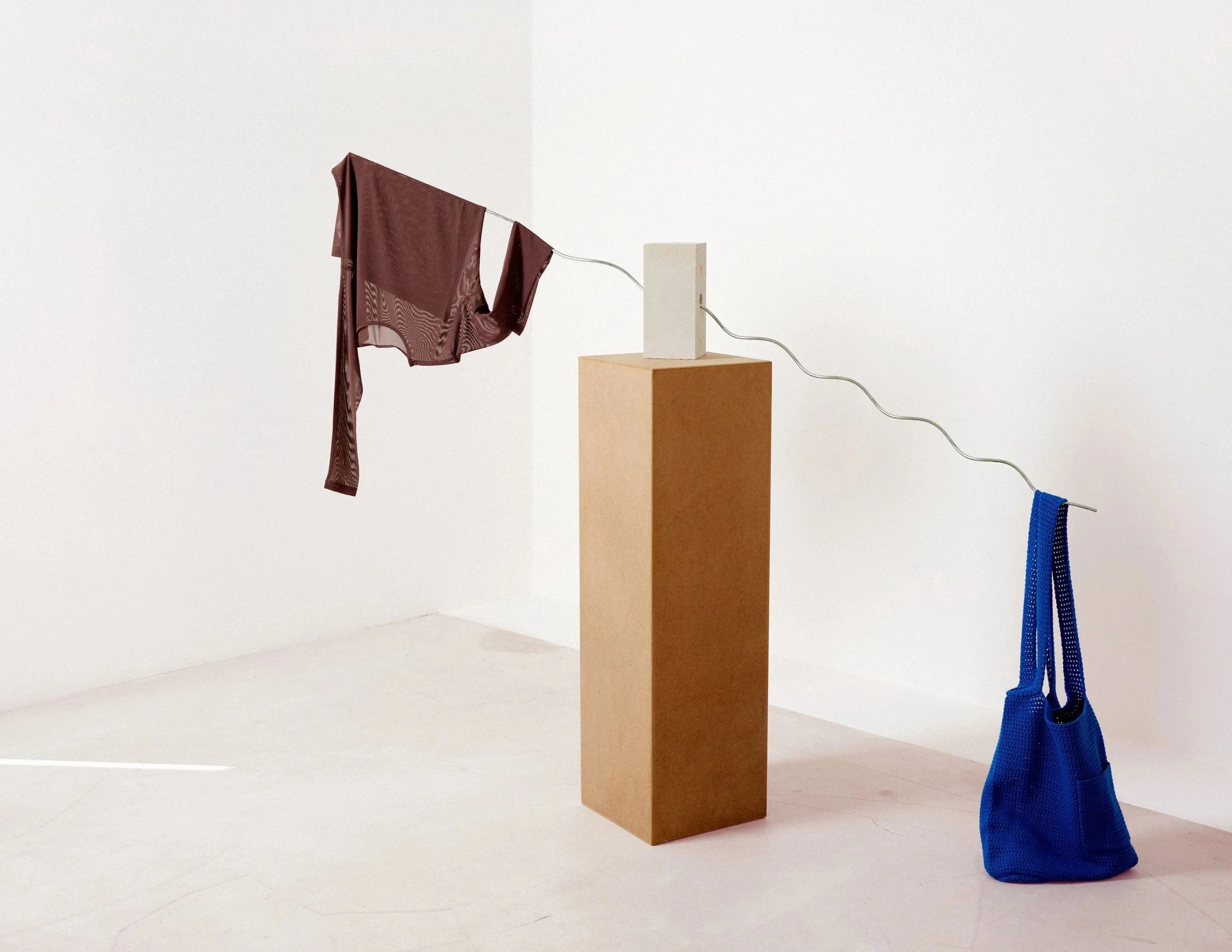 Editorial still life with garment draped across pedestal and blue bag on floor, art direction and styling by Steffi Bühlmaier for magazine editorial, photography by jessica grossmann