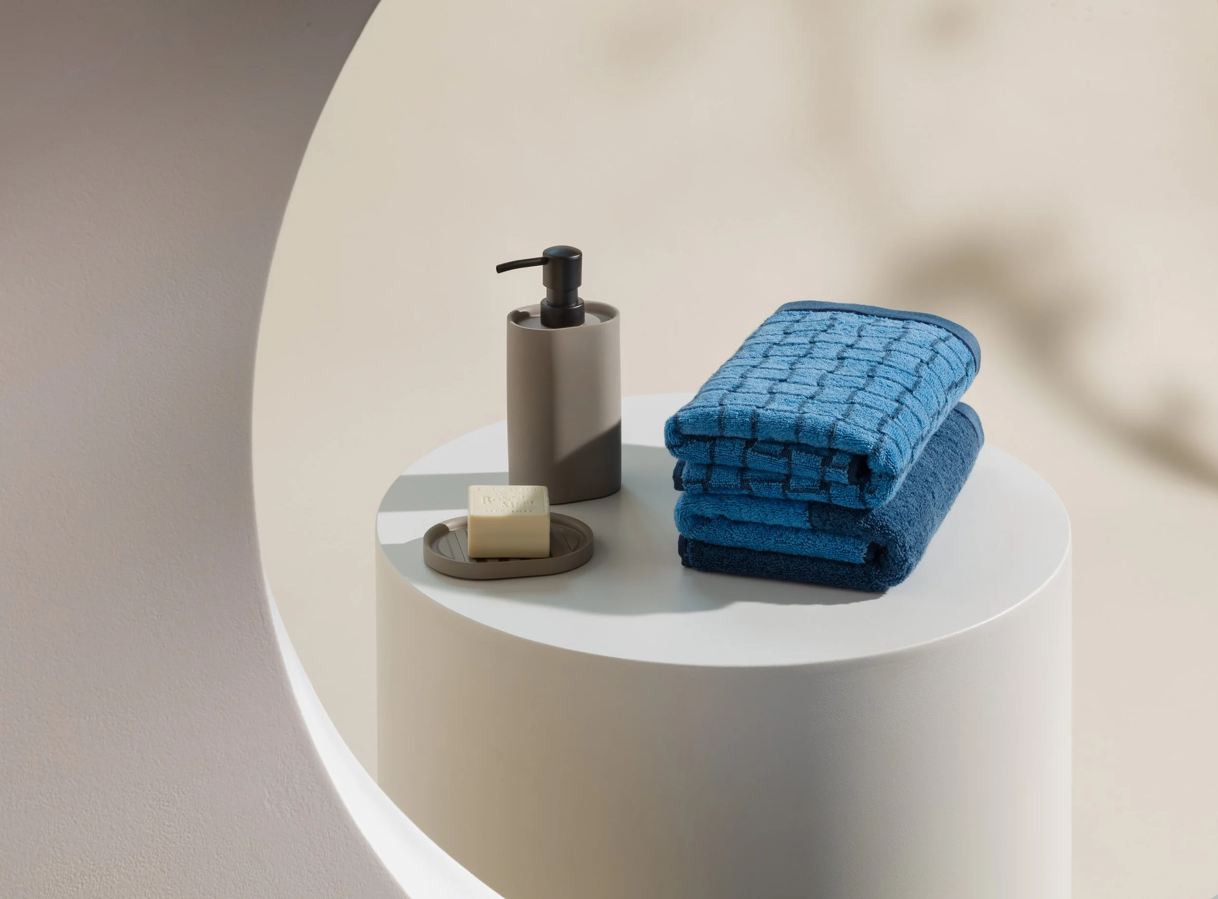 Bathroom still life with folded blue towels and soap on pedestal, set design and props styling by Steffi Bühlmaier for Möve, photography by michael tewes