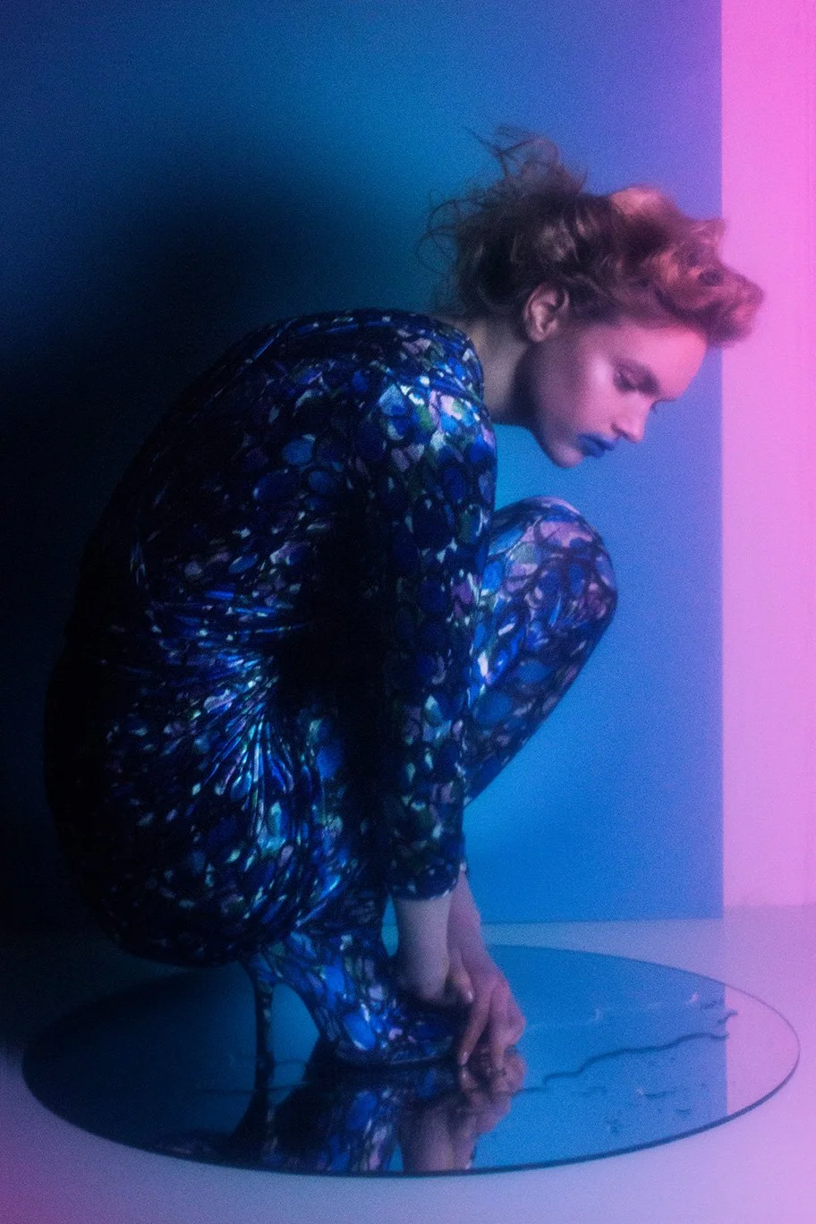 Editorial fashion image featuring crouching figure in iridescent bodysuit on mirrored surface with gradient lighting, set design and props styling by Steffi Bühlmaier, photography by Loreen Hinz for Vision Magazine China, 2019