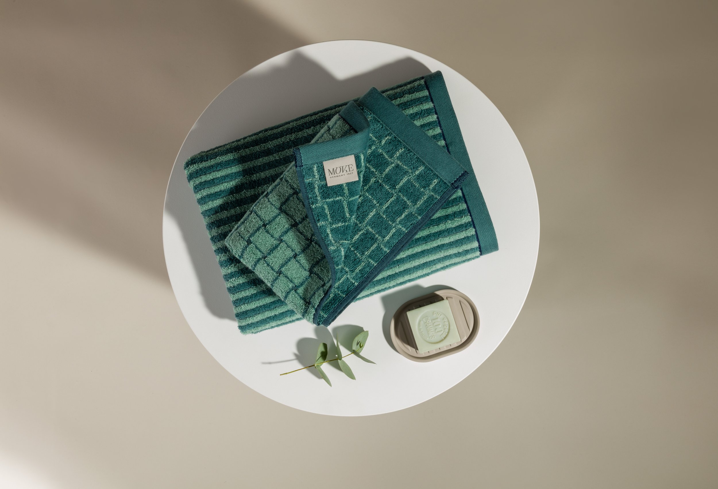 Still life featuring textured towels and soap placed on round pedestal, set build and props styling by Steffi Bühlmaier, photography by Michael Tewes, creative direction by Studio Kühn for Möve, 2025