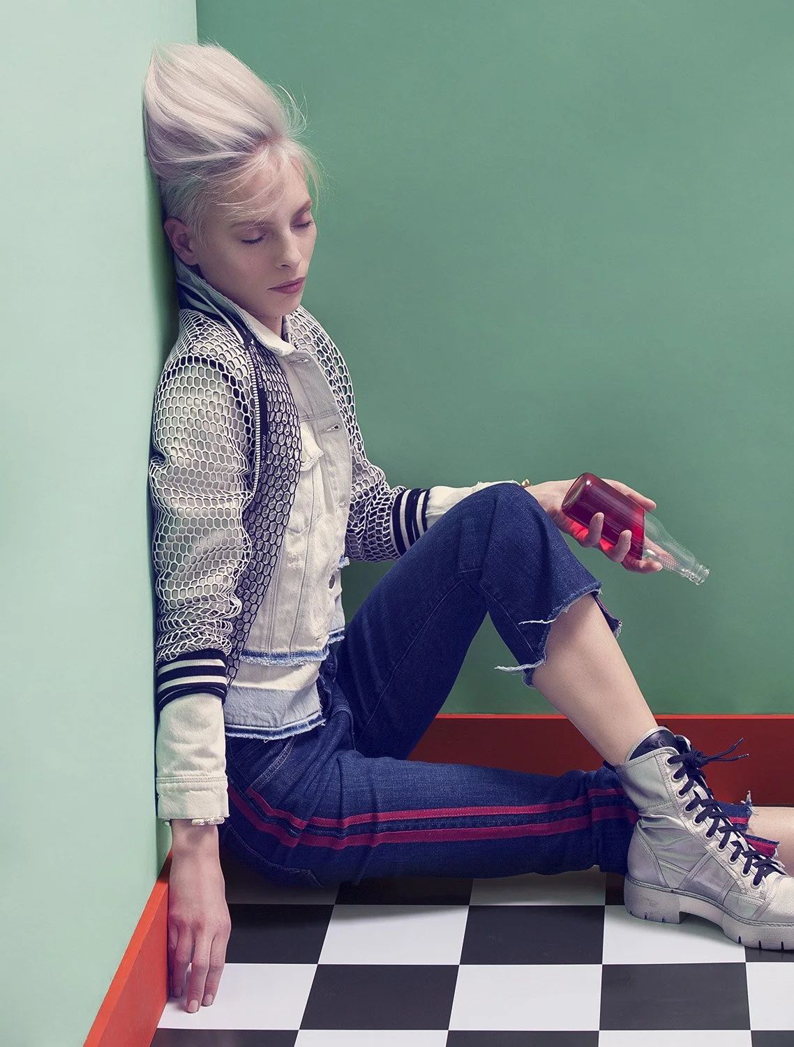 Editorial fashion image featuring seated model holding red bottle in structured jacket and boots, set design and prop styling by Steffi Bühlmaier, photography by Christina Sandrock for Jolie, 2016