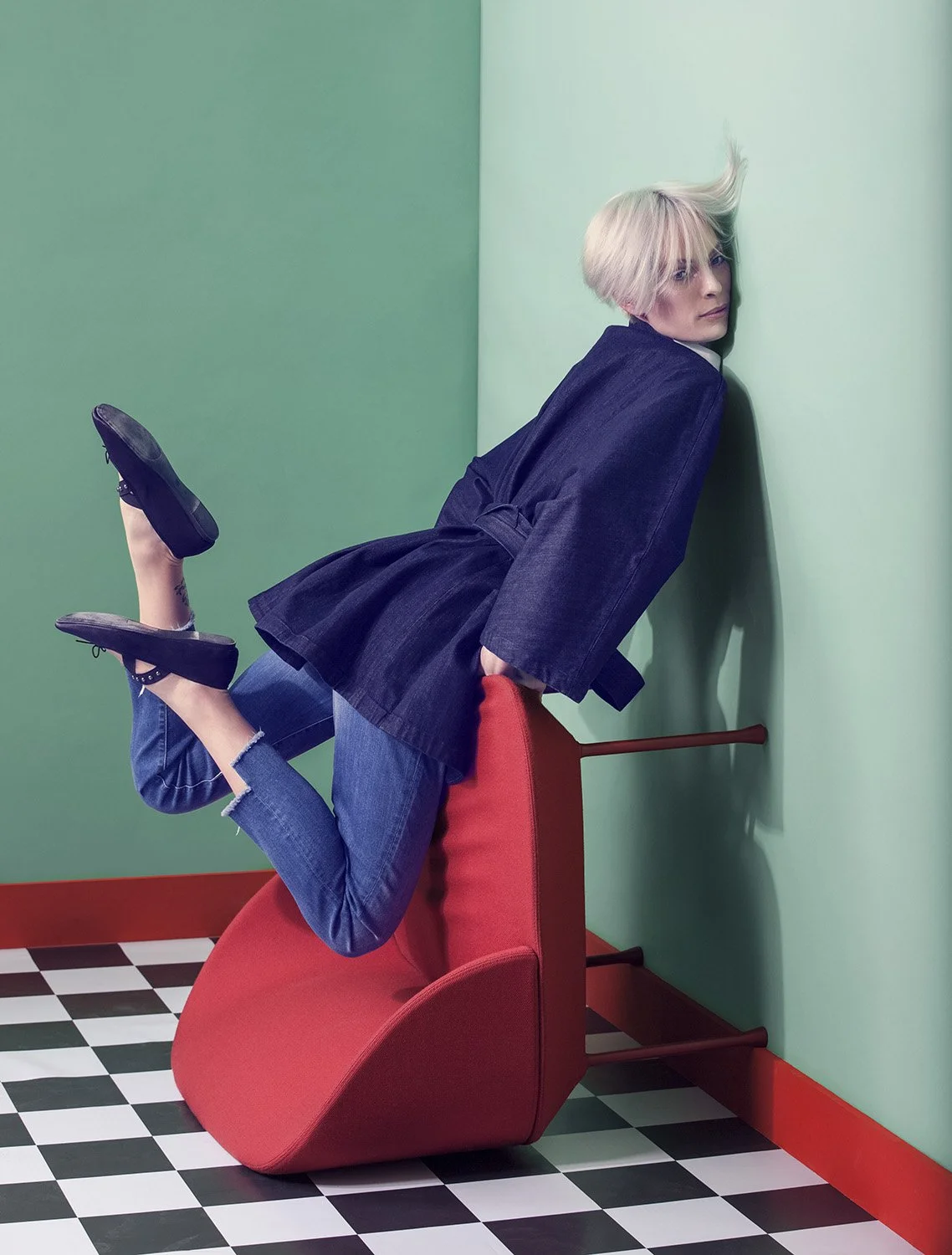 Editorial fashion image featuring model leaning forward over inverted red chair in sculptural pose, set design and prop styling by Steffi Bühlmaier, photography by Christina Sandrock for Jolie, 2016