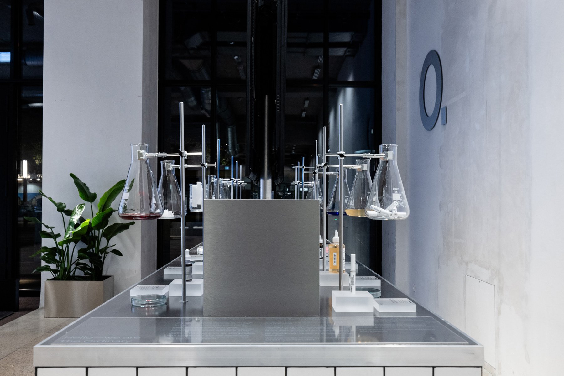 Symmetrical showroom installation with lab-inspired display elements and illuminated vessels presenting skincare products, display design and props styling by Steffi Bühlmaier for The Ordinary x Highsnobiety temporary showroom, event production by PS