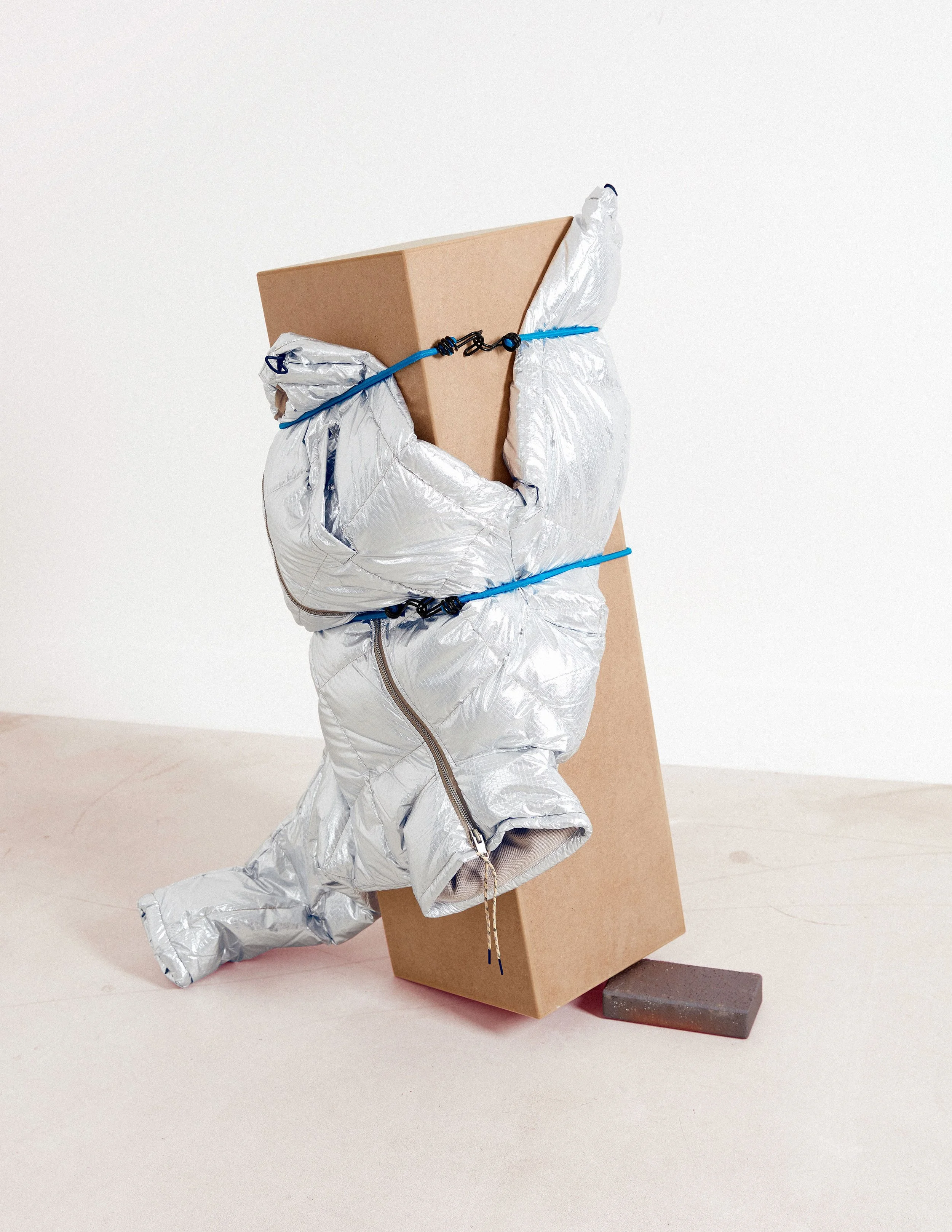 Editorial still life composition with silver padded jacket fixed to pederstral
 using elastic cords, art direction by Steffi Bühlmaier, photography by Jessica Grossmann for Heyday Magazine, 2022
